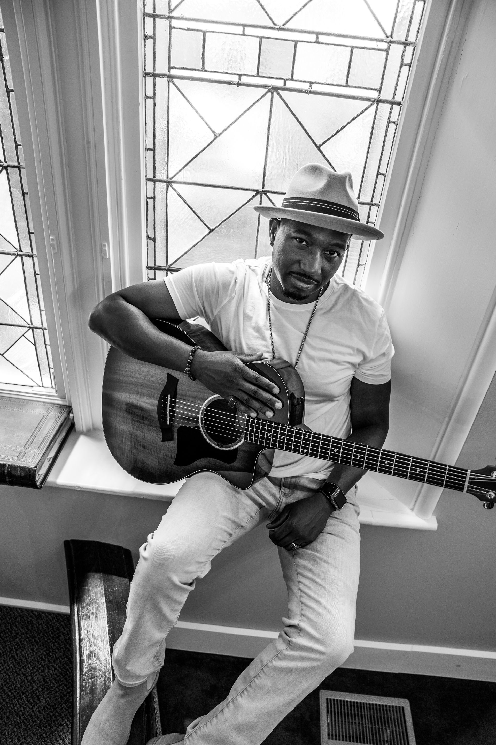 Corey Tucker is sitting on a window sill playing a guitar.