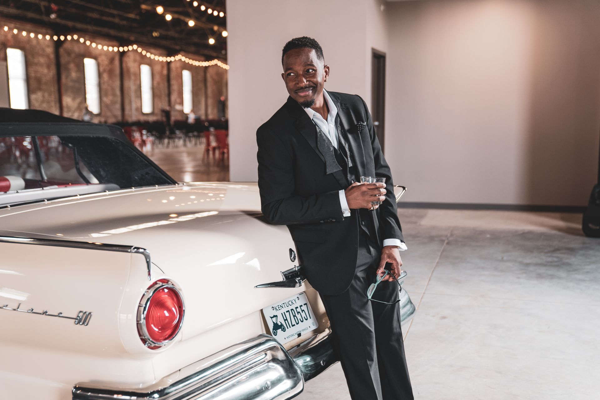 Corey Tucker in a suit is standing next to a white car.