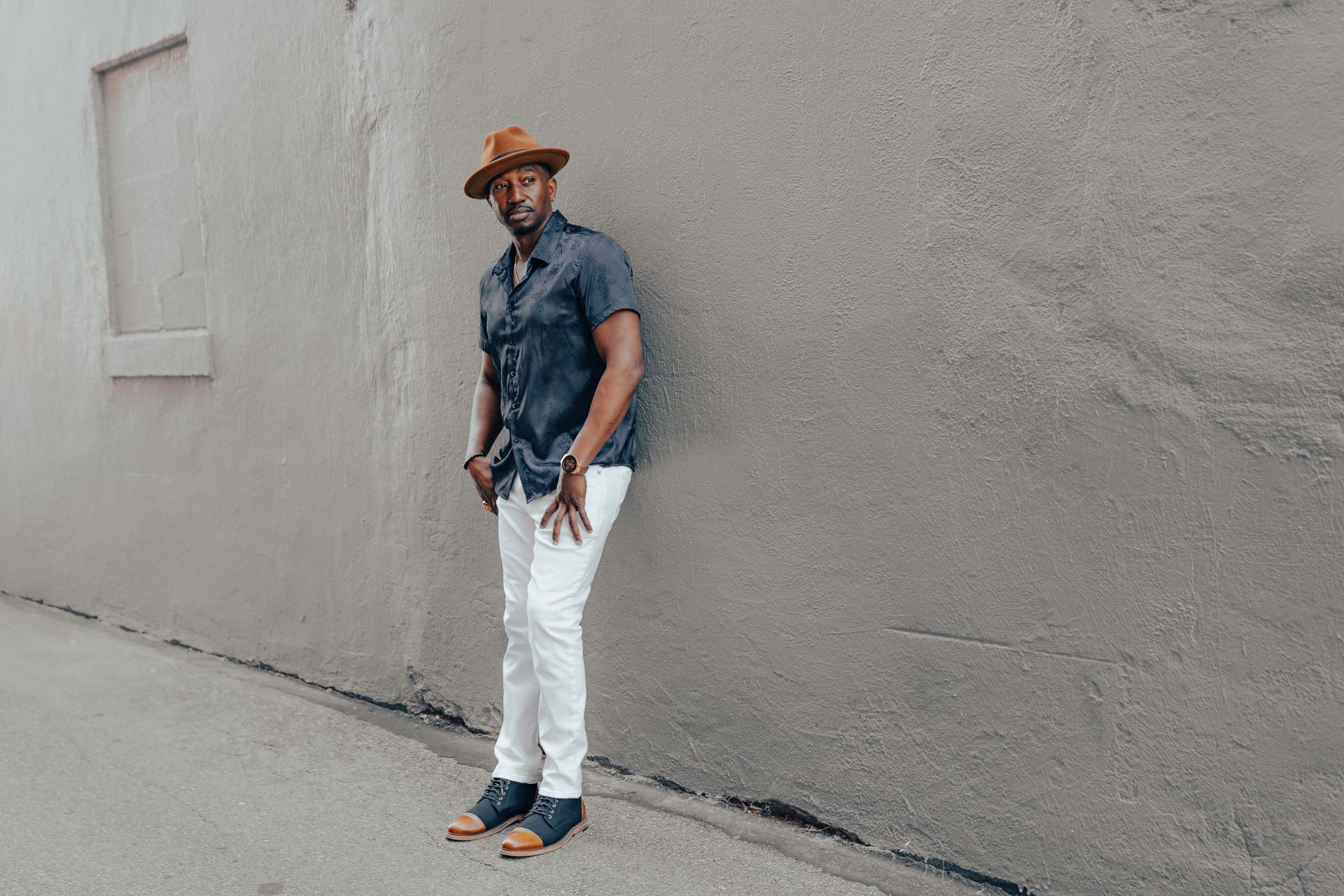 Corey Tucker in a hat is leaning against a wall.