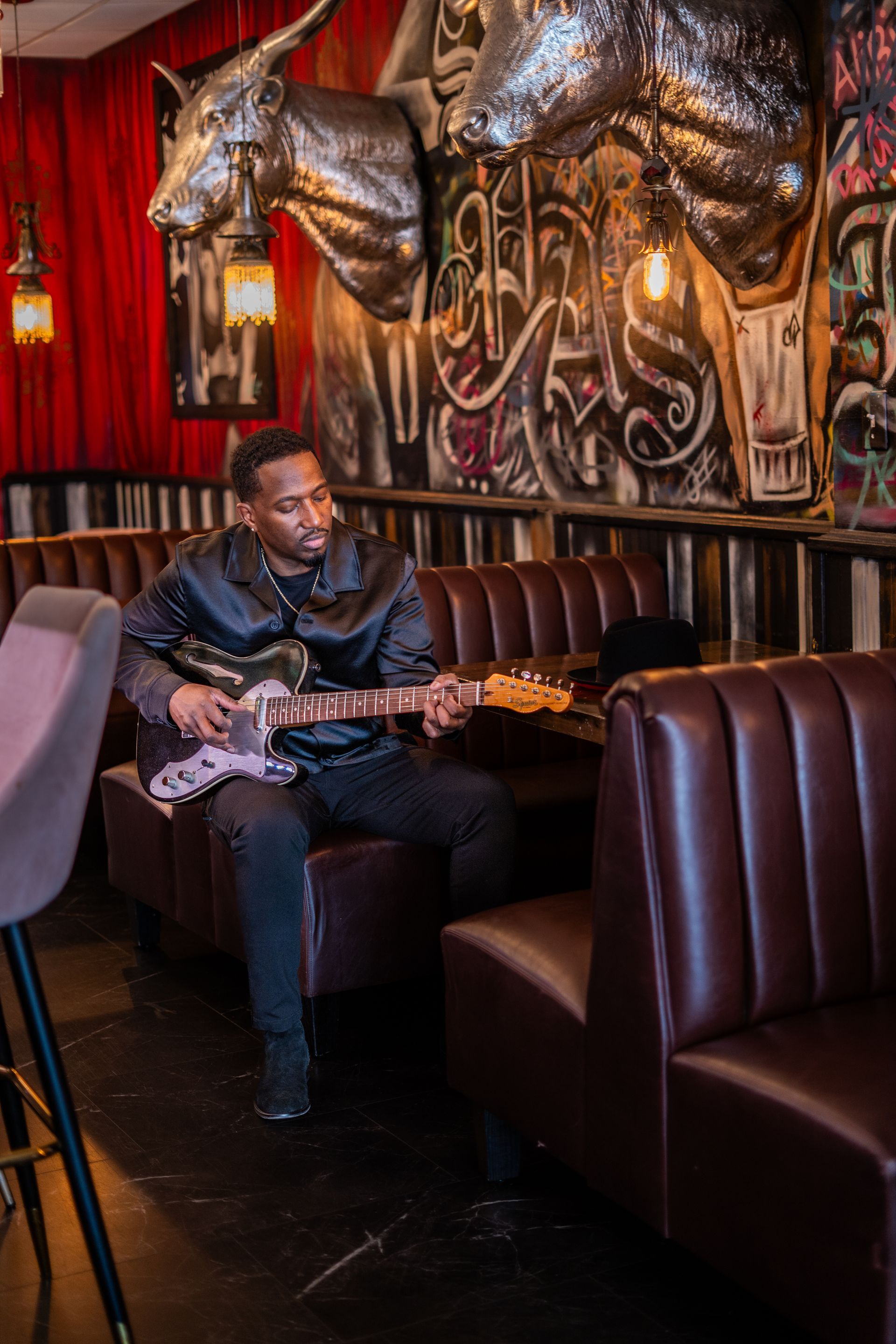 Corey Tucker is sitting on a couch playing a guitar in a restaurant.