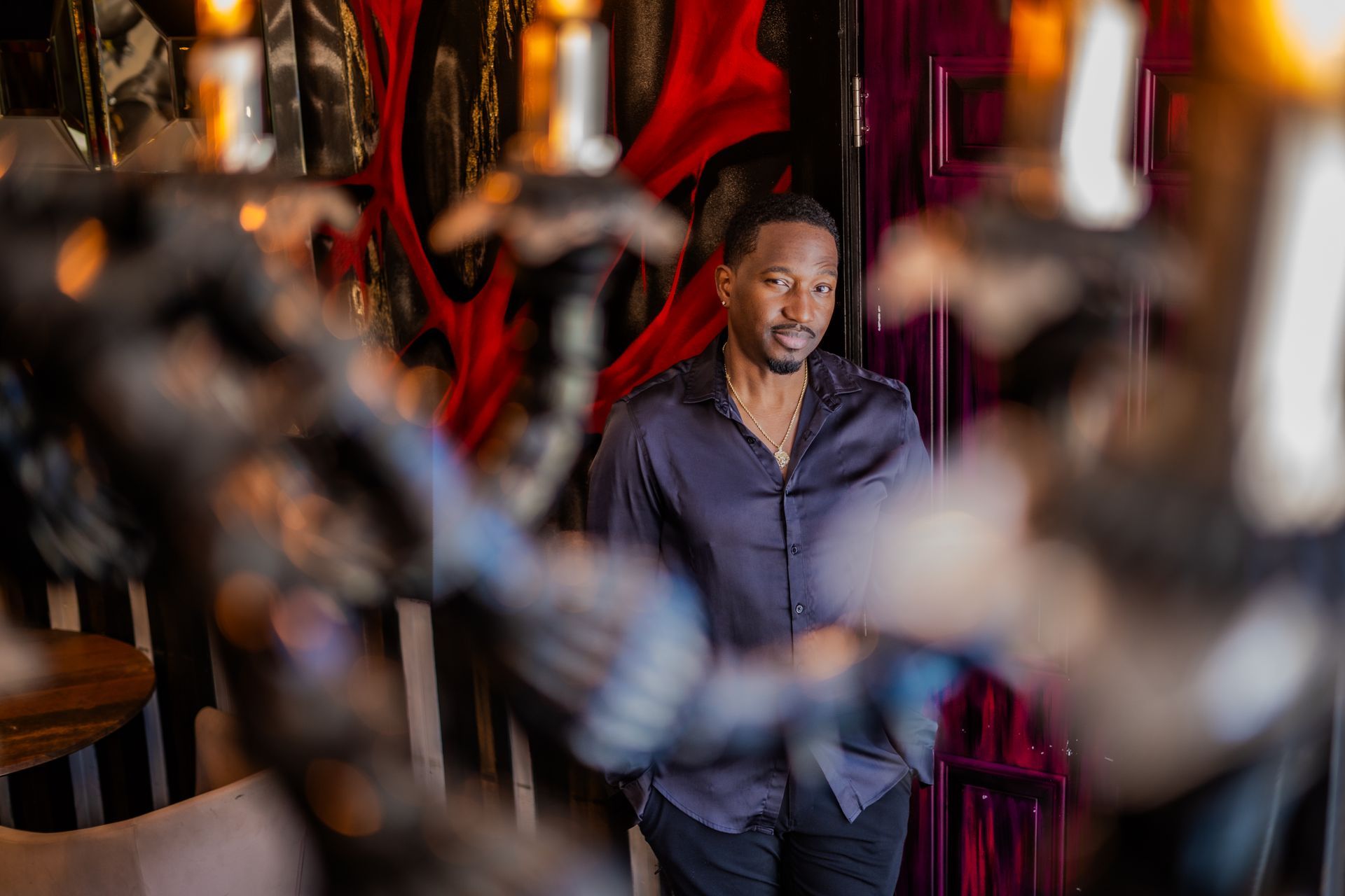 Corey Tucker in a black shirt is standing in front of a chandelier.