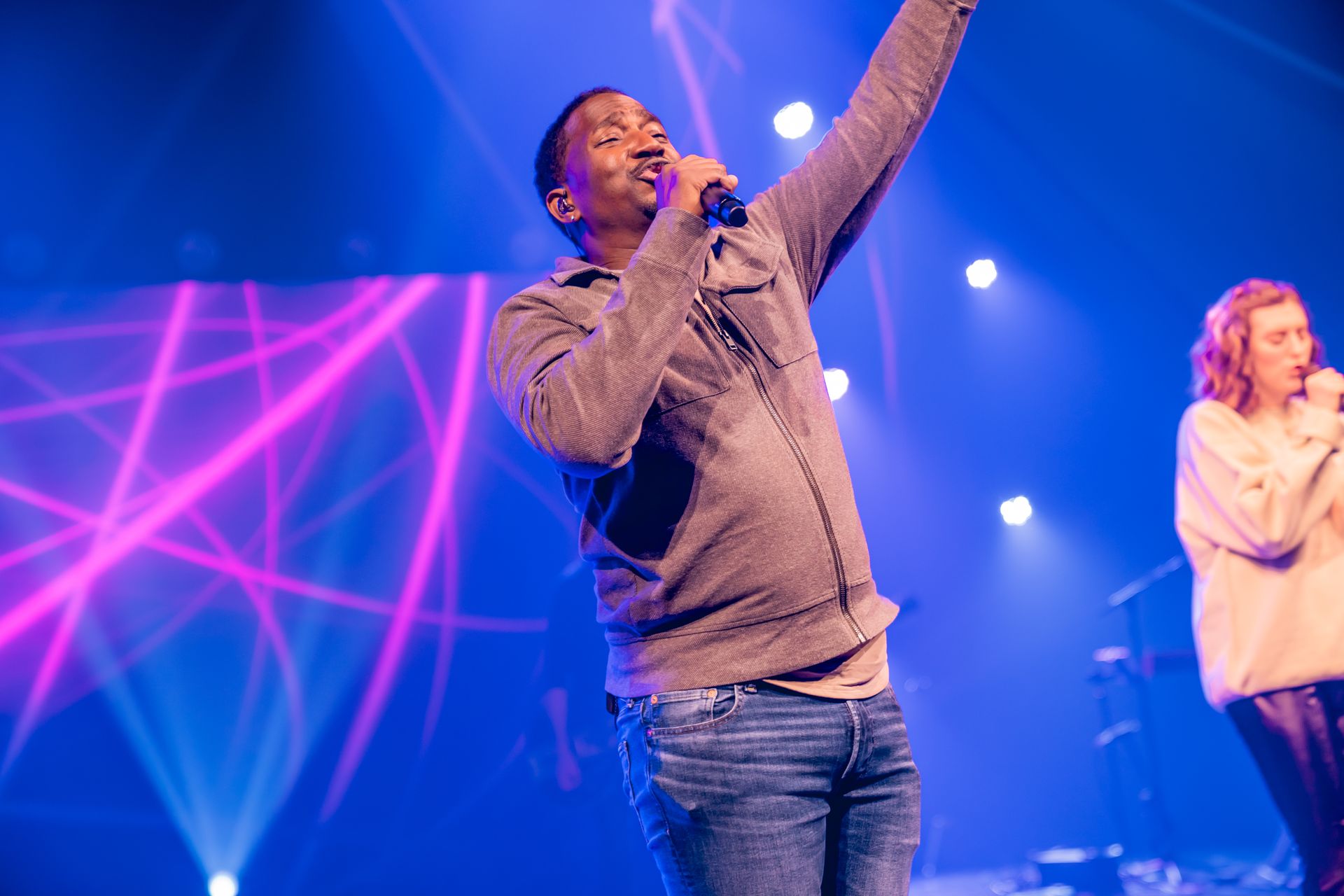 Corey Tucker is singing into a microphone on a stage.