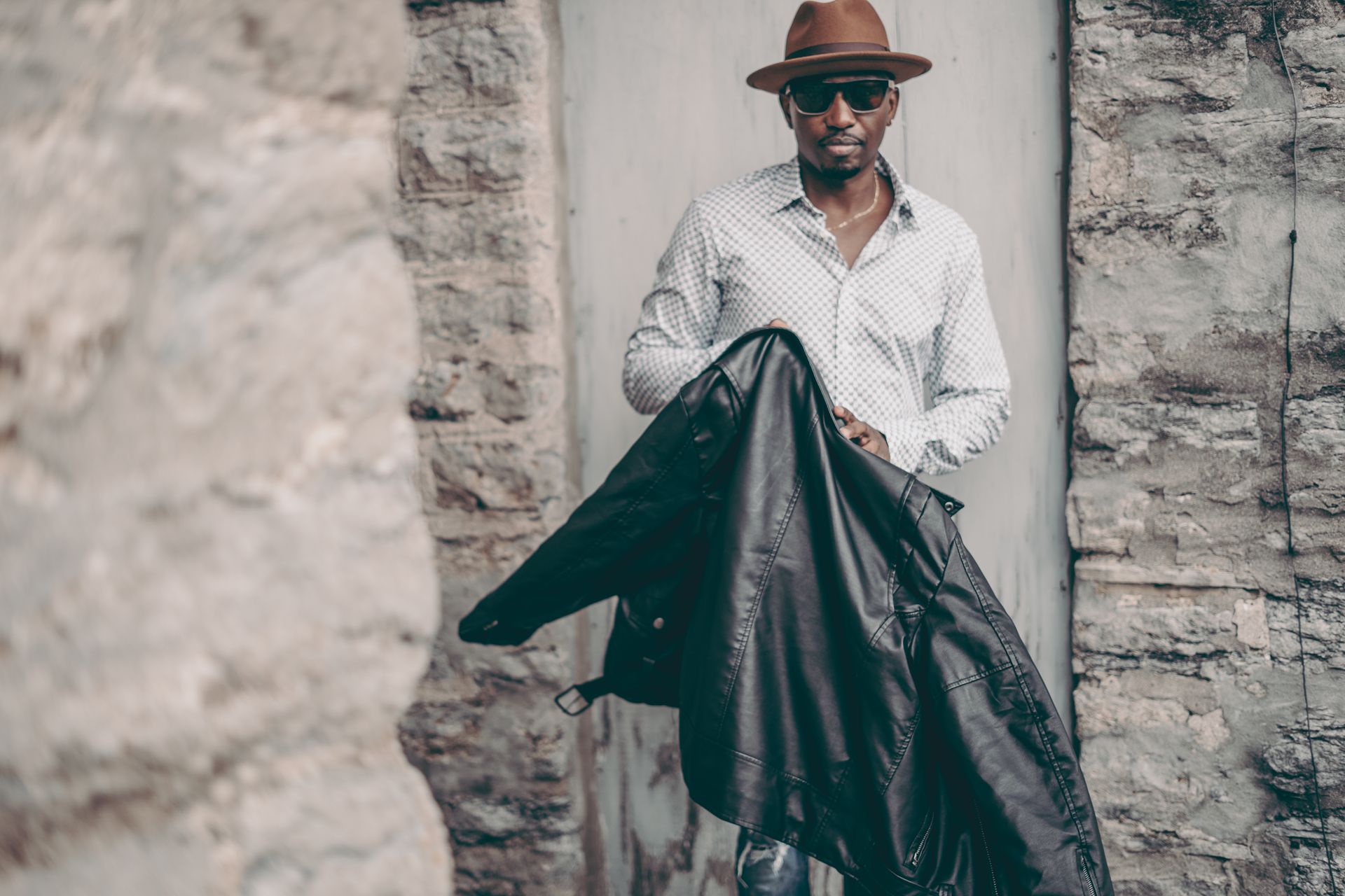 Corey Tucker wearing a hat and sunglasses is holding a black leather jacket.