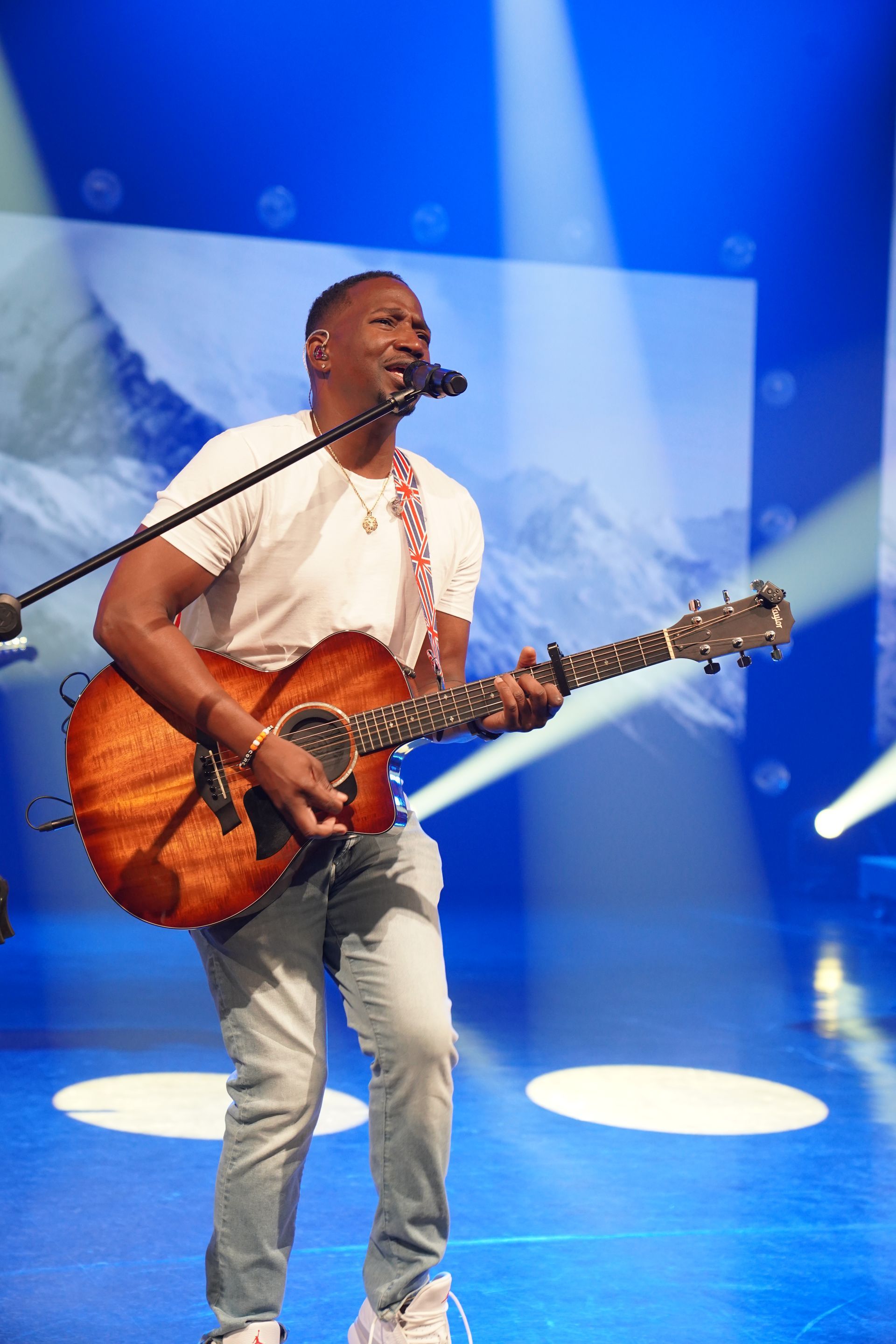 Corey Tucker is playing a guitar and singing into a microphone on a stage.
