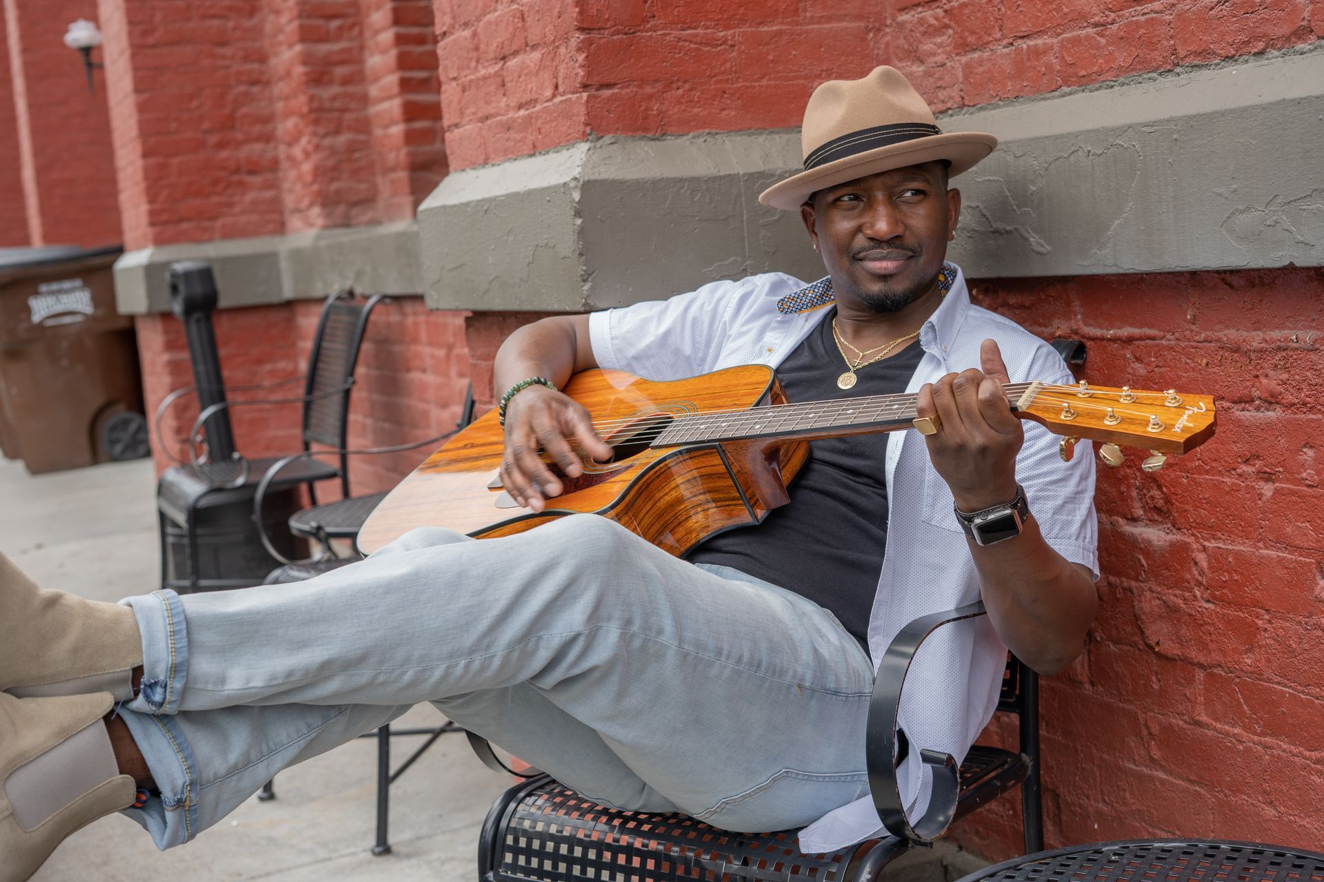 Corey Tucker is sitting on a bench playing an acoustic guitar.