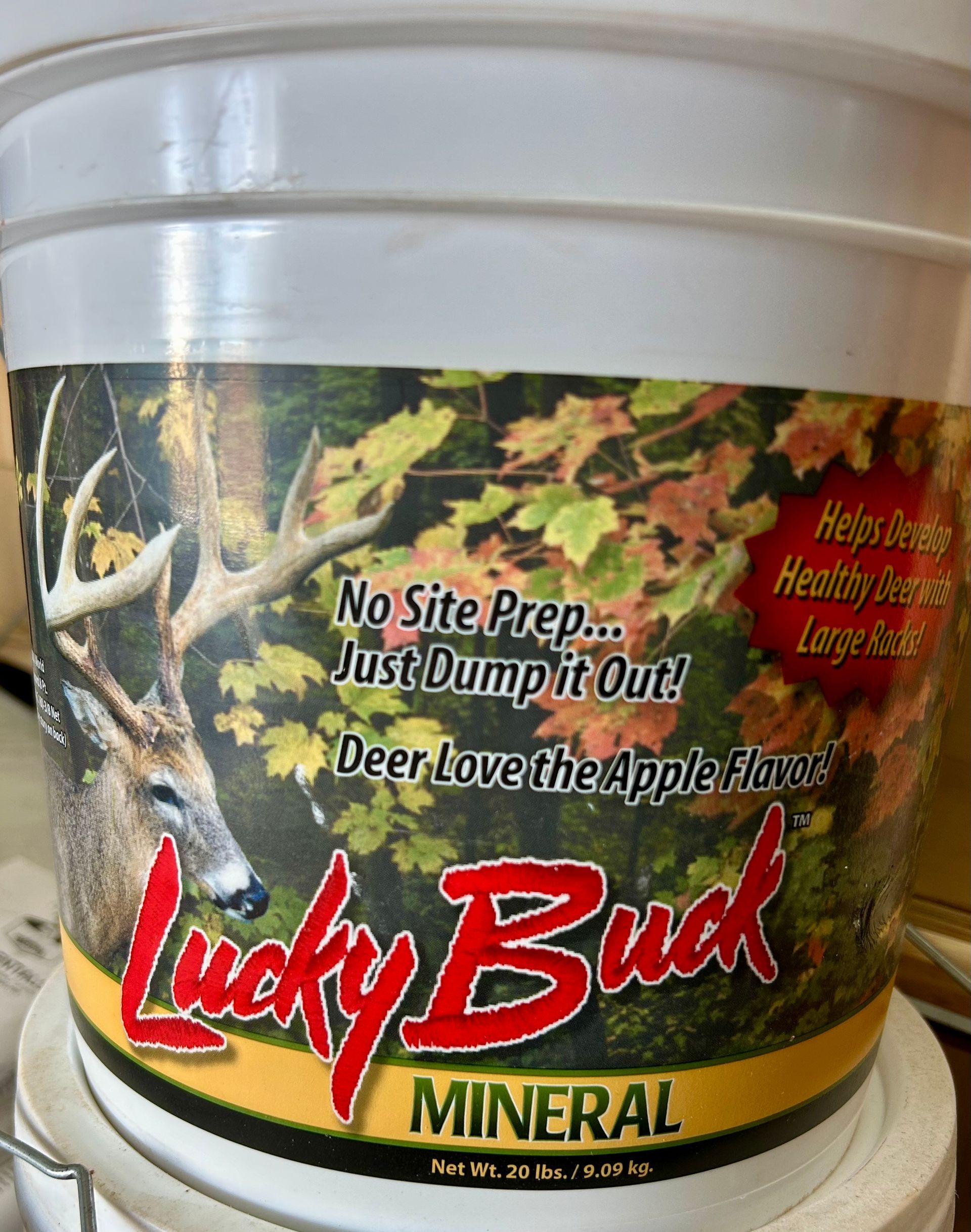 White bucket of Lucky Buck mineral deer feed. The label features a buck with antlers and fall foliage; text: 
