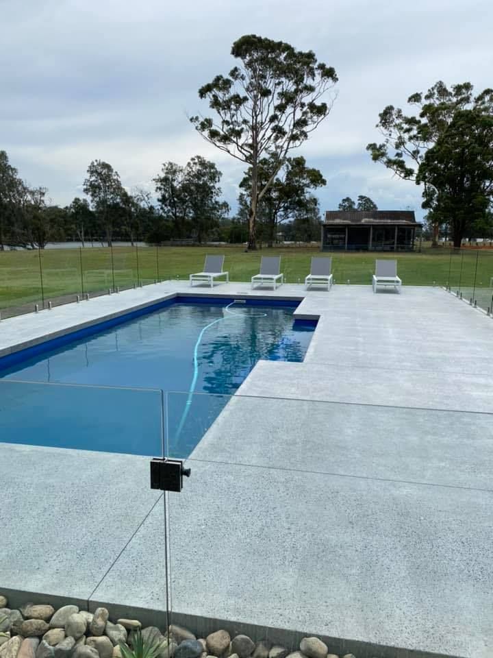 Rectangular Pool With Glass Fence, Concrete Deck, and Lounge Chairs — Williams Concreting In Taree, NSW
