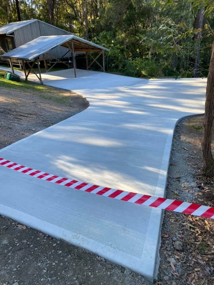 New concrete driveway with red and white barrier tape, leading to a wooden carport in a wooded area — Williams Concreting In Nabiac, NSW