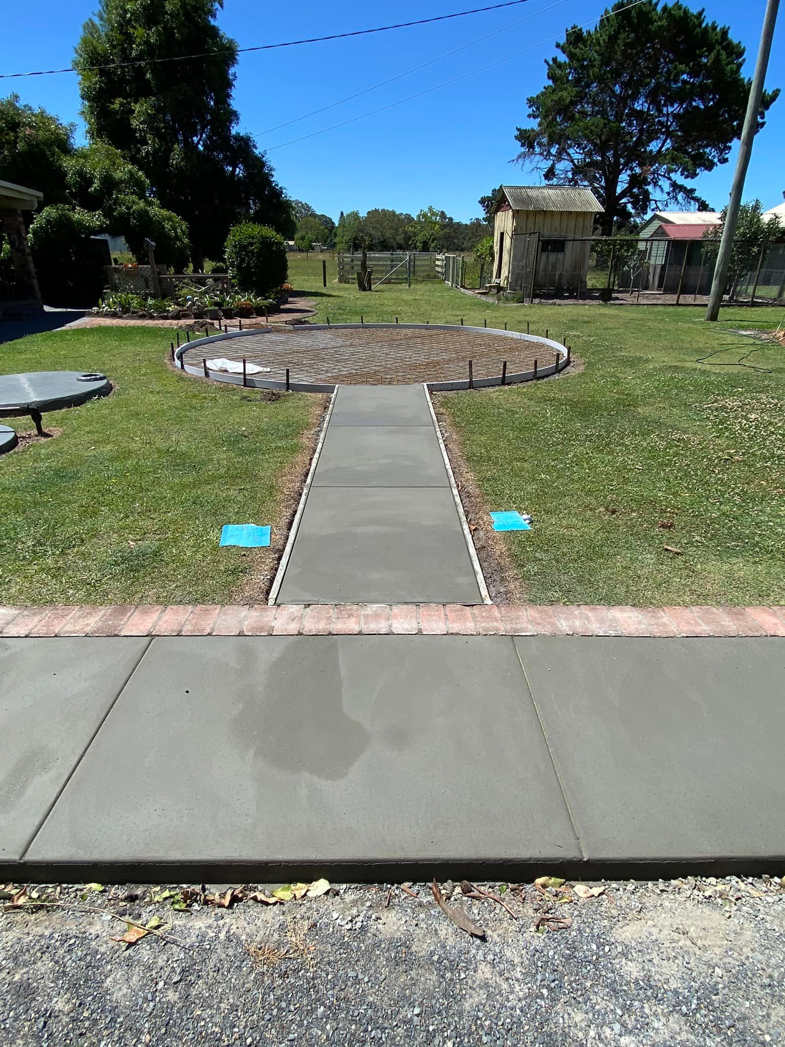 A Concrete Pathway Leads to a Garden With Grass, a Small Building, and Blue Sky — Williams Concreting In Taree, NSW