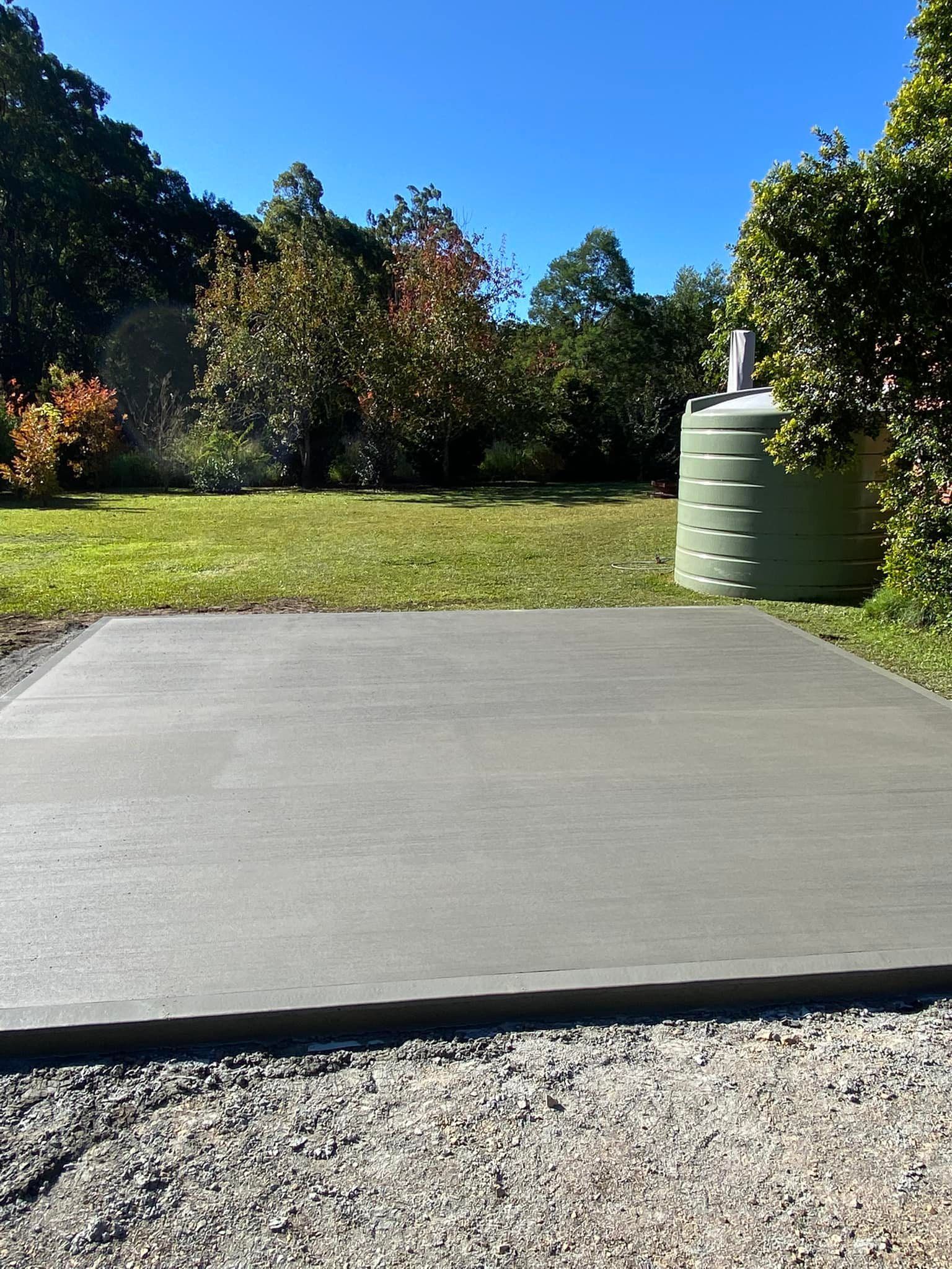 A freshly Poured Concrete Slab on Gravel, Green Tank, Backyard With Trees, Blue Sky — Williams Concreting In Taree, NSW