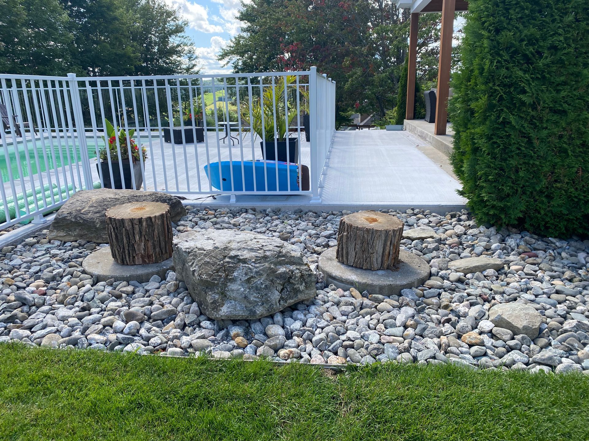 Un jardin avec des rochers et une souche devant une piscine.