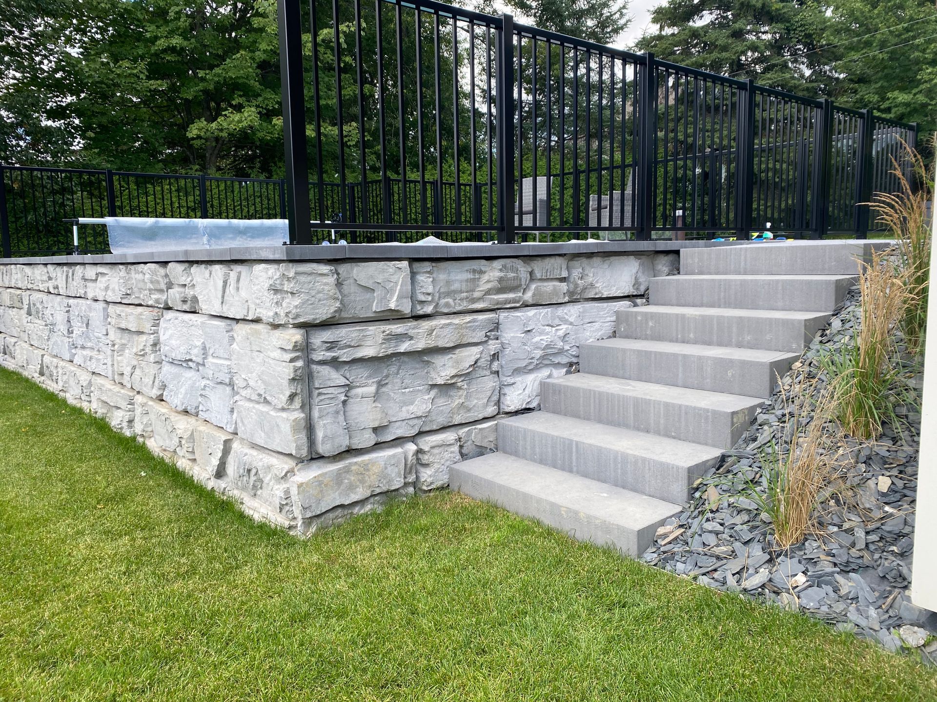Un mur de pierre avec des escaliers qui y mènent et une clôture noire.