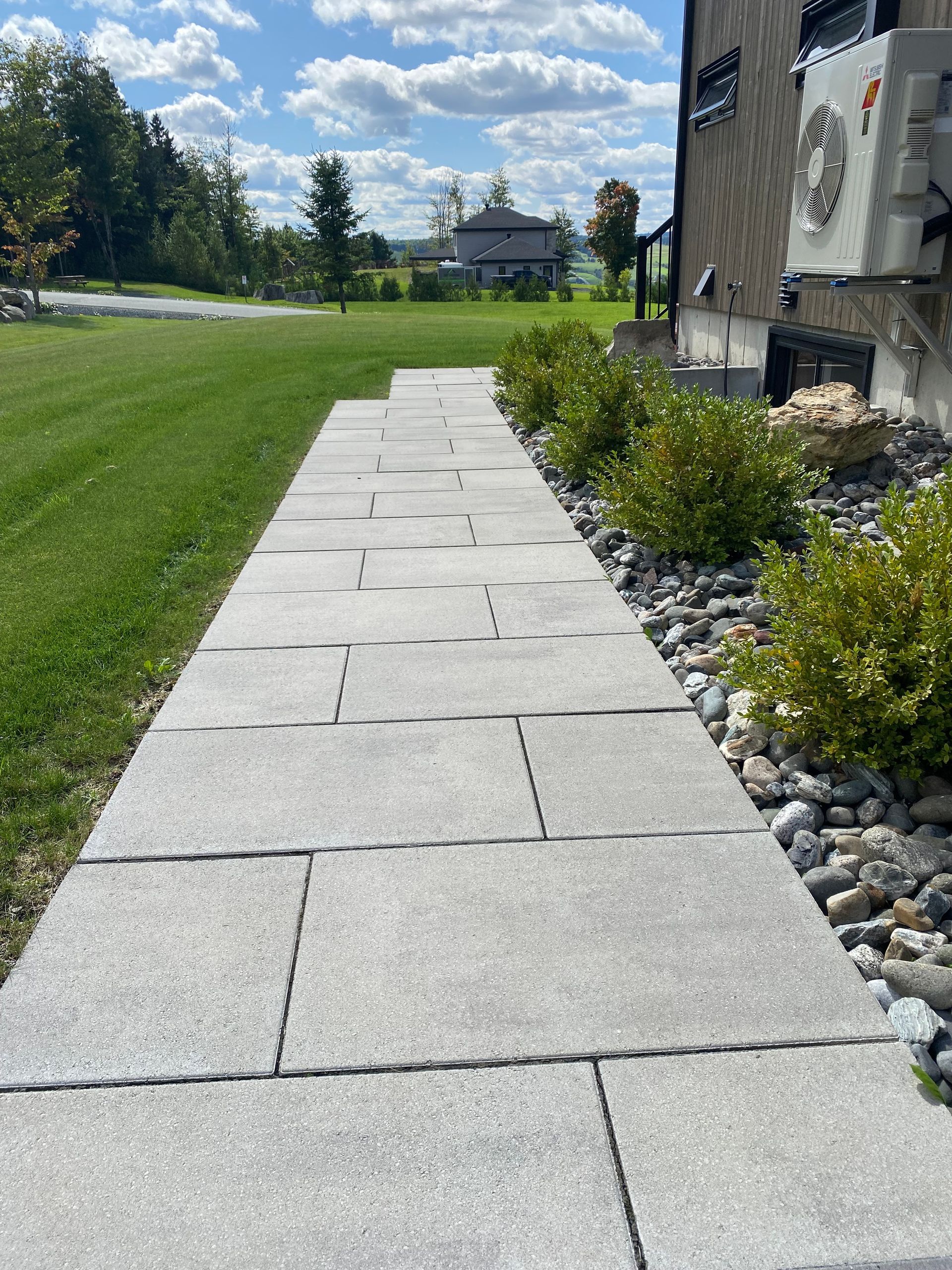 Un trottoir menant à une maison avec beaucoup d'herbe et de rochers