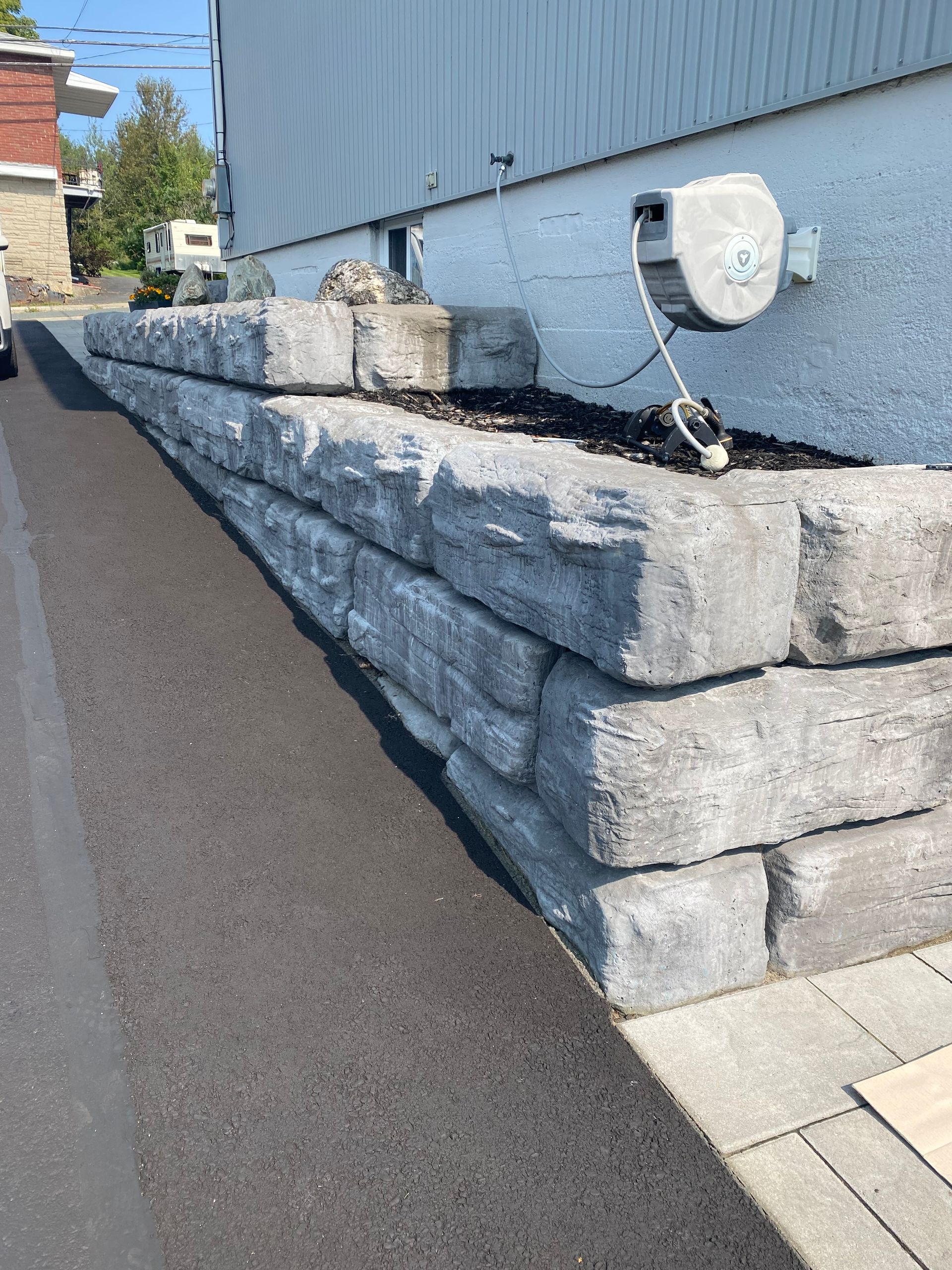 Un grand mur de pierre le long d'une route à côté d'une maison.