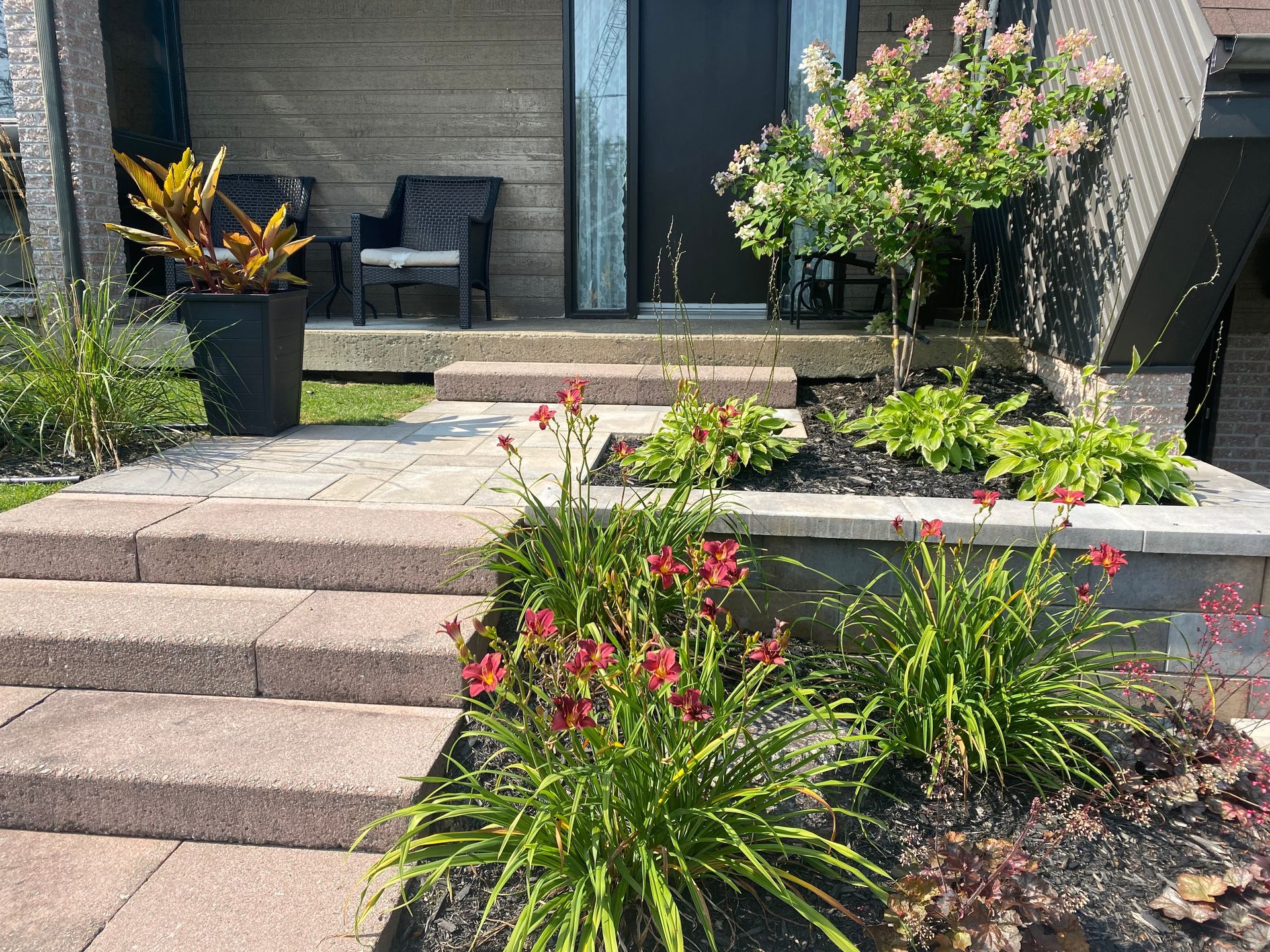 Une allée en briques menant à la porte d'entrée d'une maison entourée de fleurs et de plantes.
