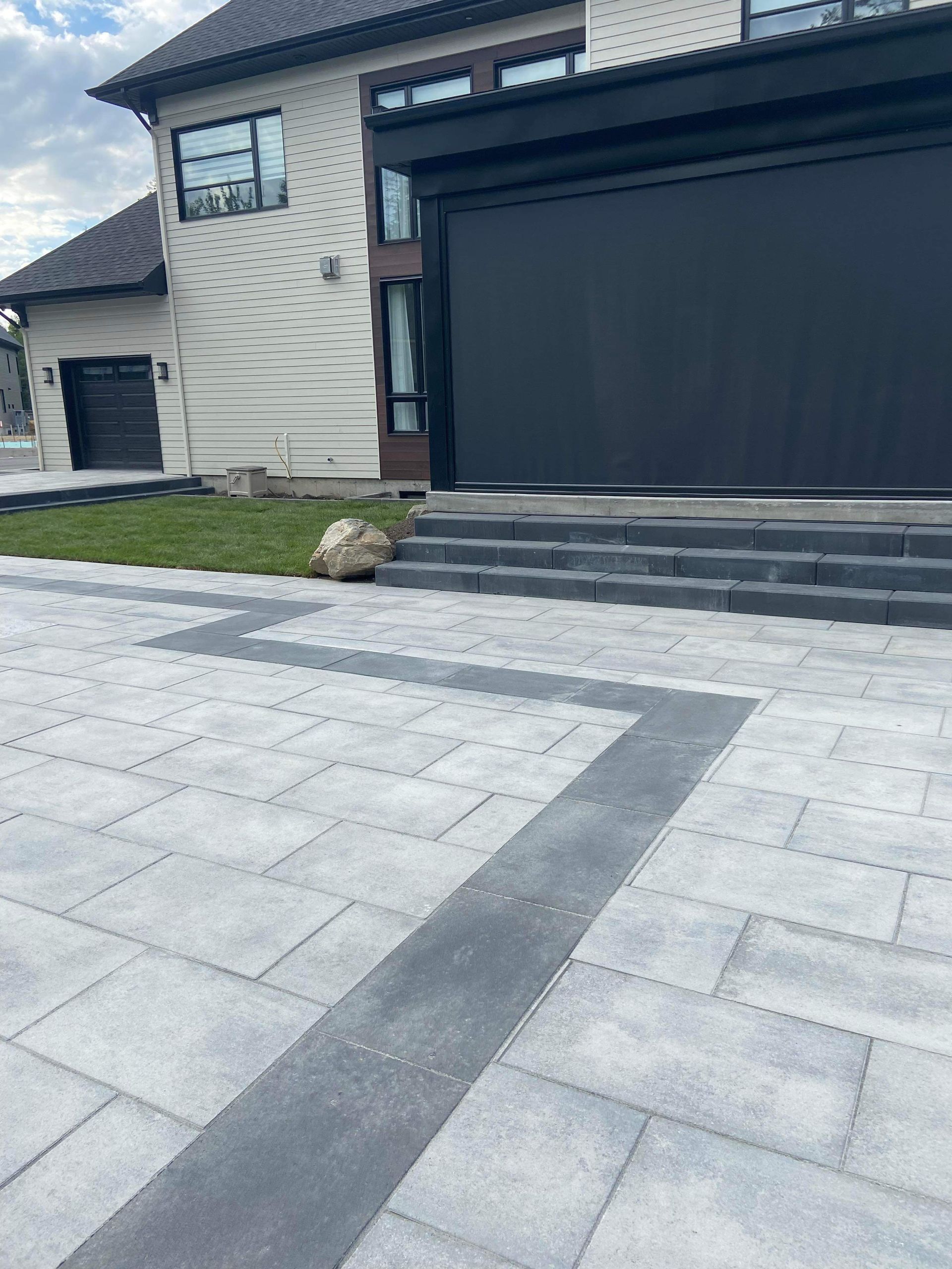 Une grande maison avec une porte de garage noire et une allée en béton devant.