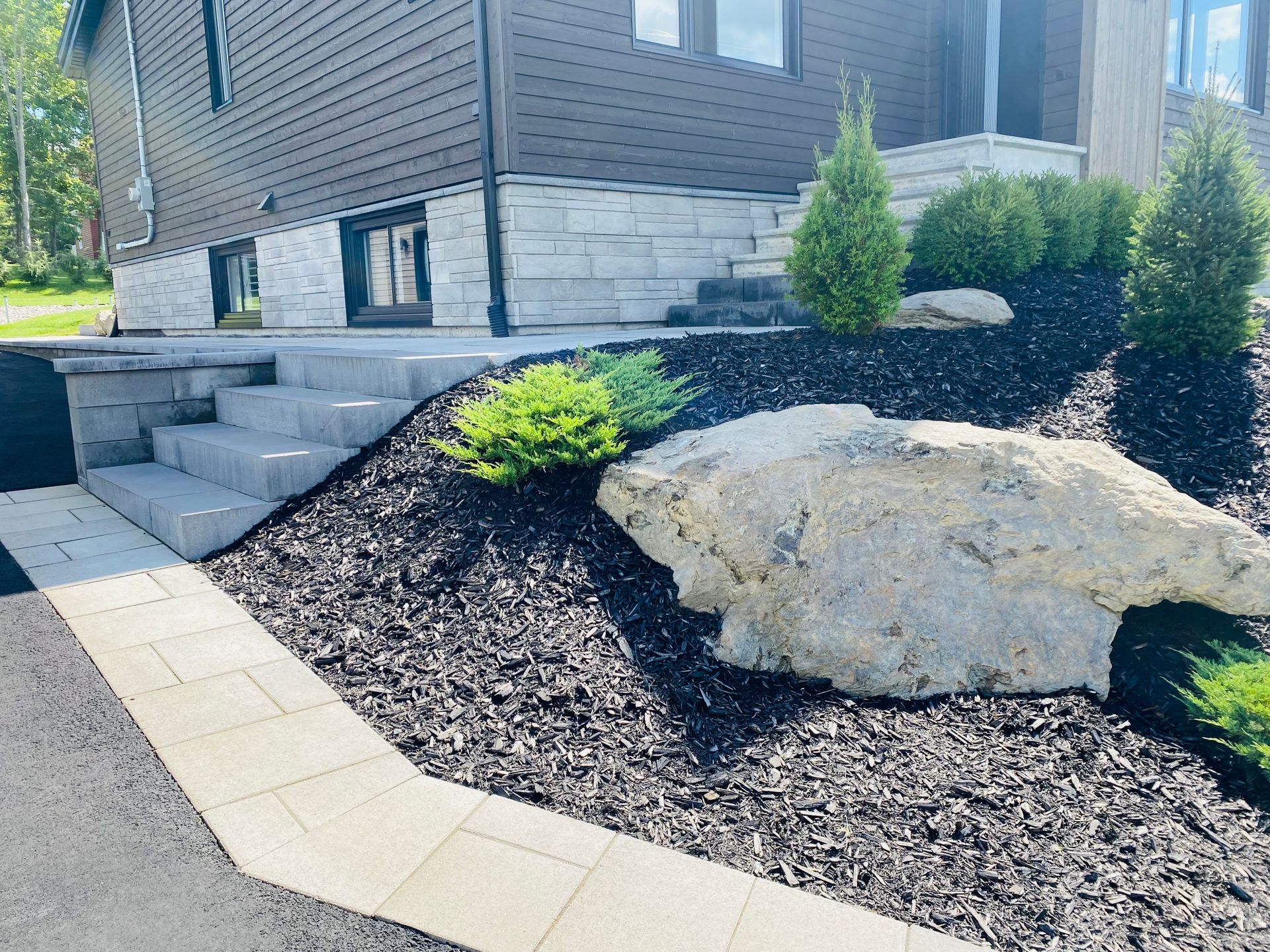 Une maison avec des escaliers et un gros rocher devant.