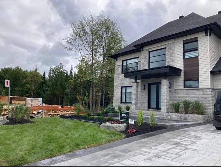 Une grande maison blanche avec un toit noir est assise au sommet d'une pelouse verte luxuriante.