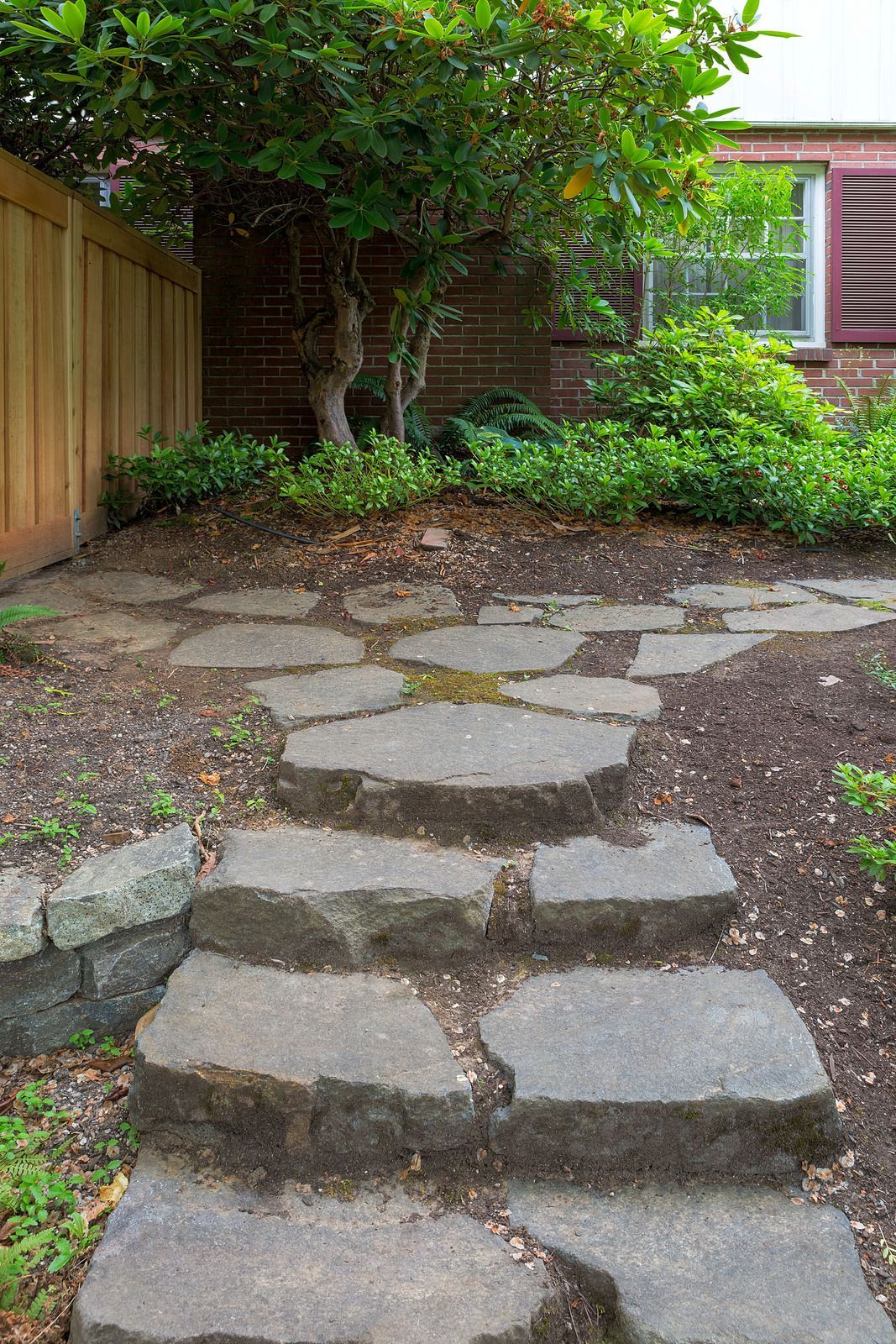 A stone walkway leading to a house with a wooden fence.