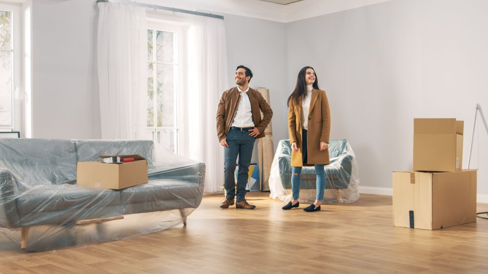 A Man And A Woman Are Standing In A Living Room With Cardboard Boxes — Settle Petal Mobile Conveyancing In Wallabi Point, NSW