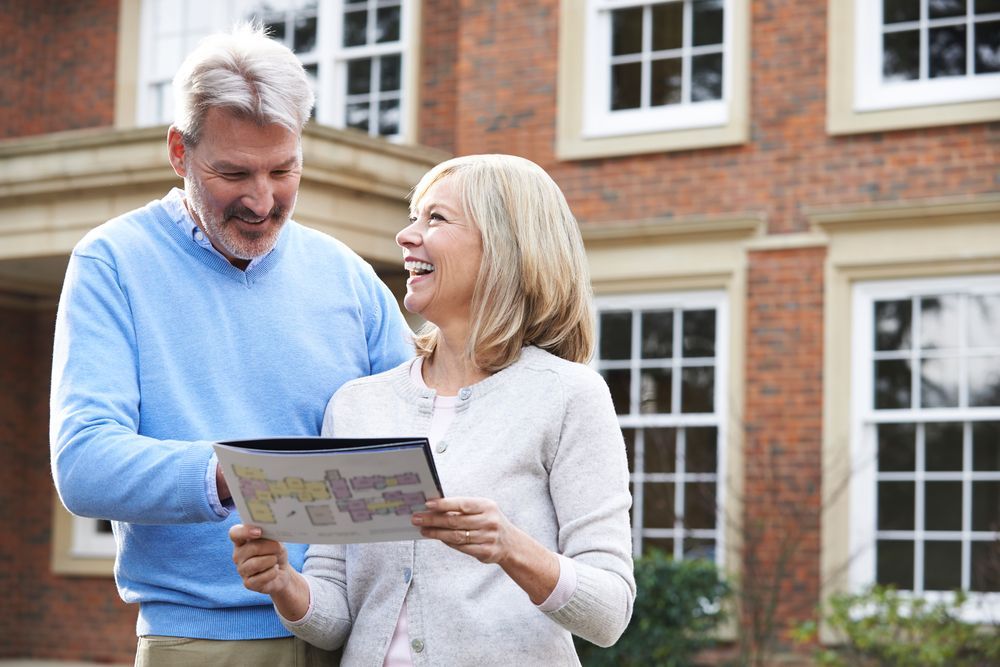 A Man And A Woman Are Standing In Front Of A Brick House Looking At A Map — Settle Petal Mobile Conveyancing In Wallabi Point, NSW