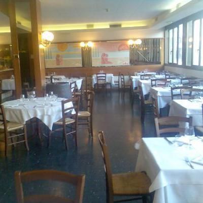Interno di un ristorante con tavoli coperti da tovaglie bianche e sedie in legno.