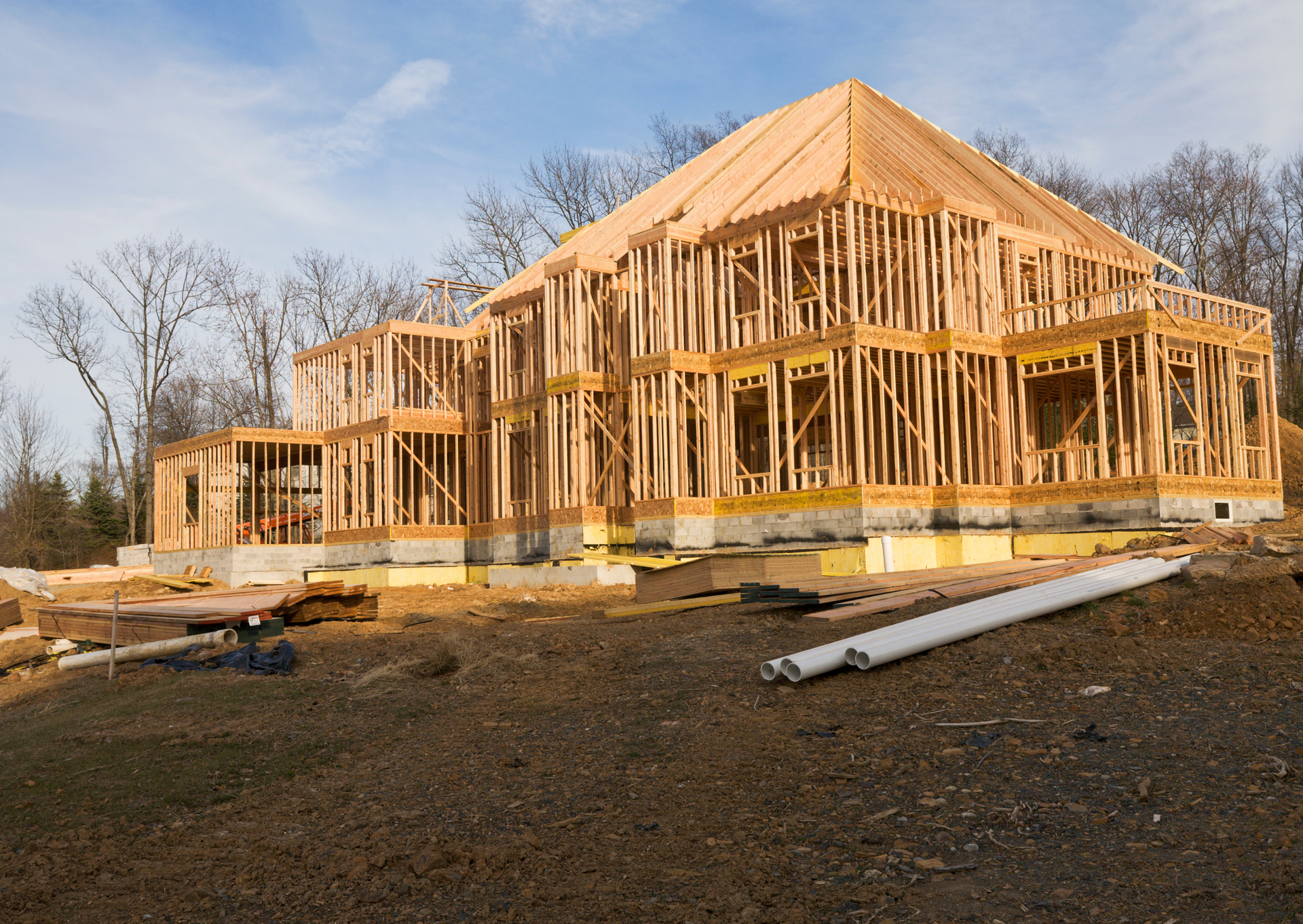 A large wooden house is being built in the middle of a dirt field.