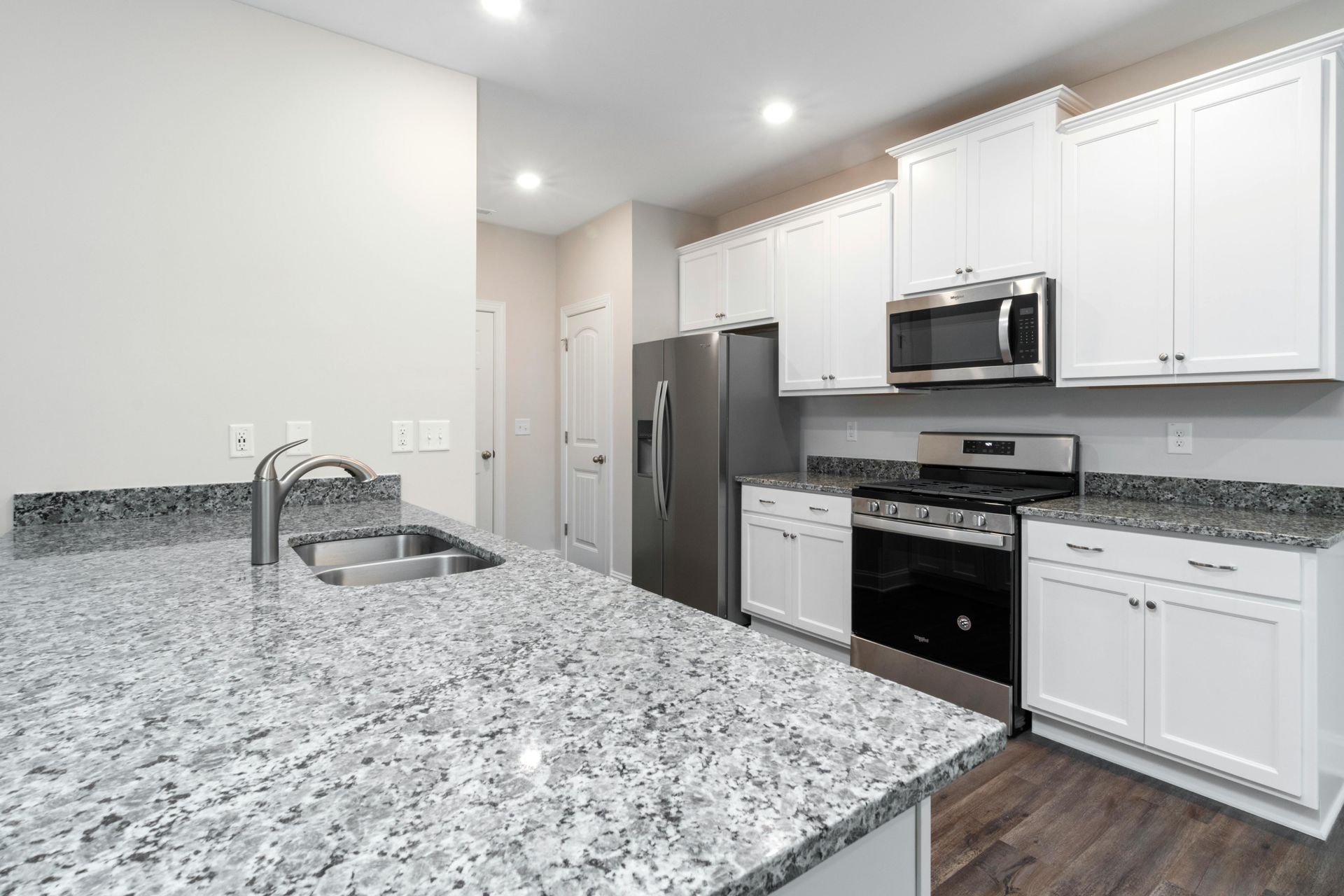 Modern kitchen with white cabinets, stainless steel appliances, granite countertops, and dark flooring.