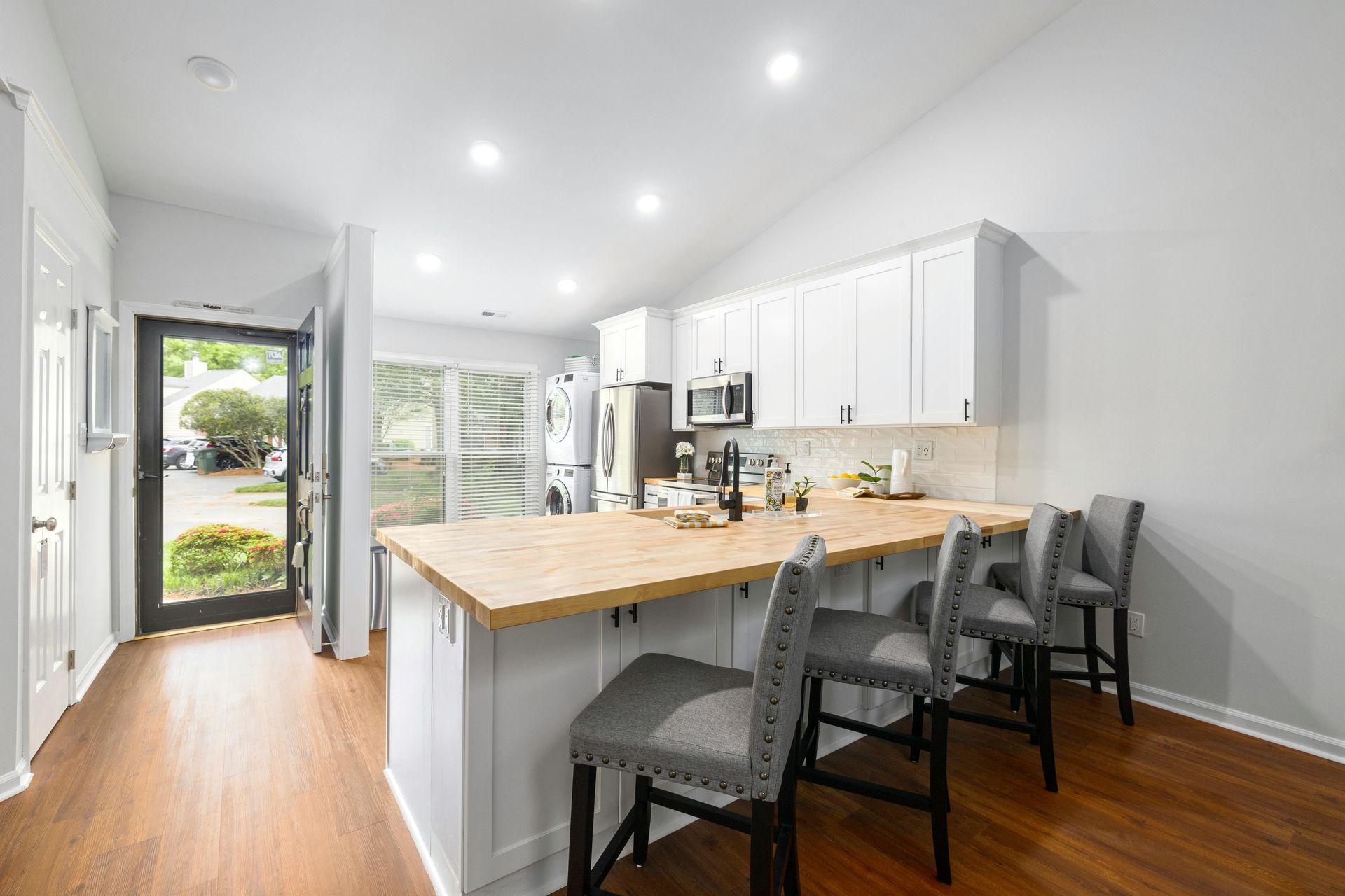 Kitchen with white cabinets, wood countertops, and gray bar stools.