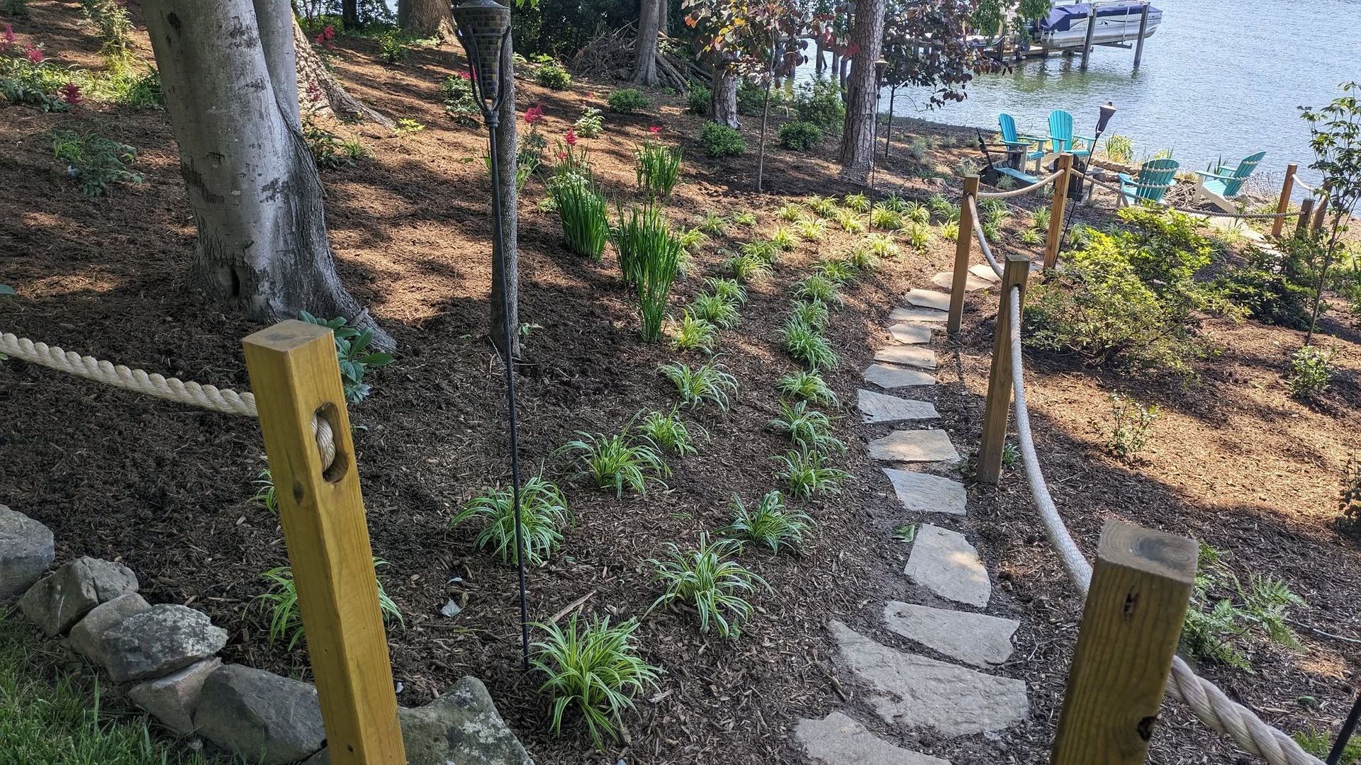 Stone path descends a landscaped hillside towards water, flanked by rope and wooden posts.