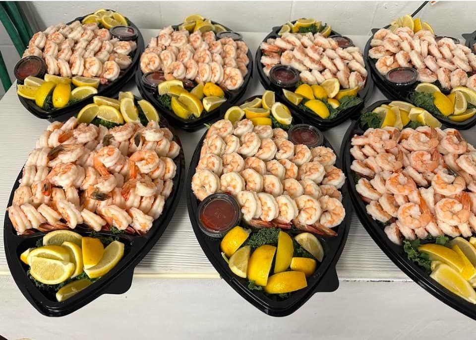 Eight platters of cooked shrimp with lemon wedges and sauce.