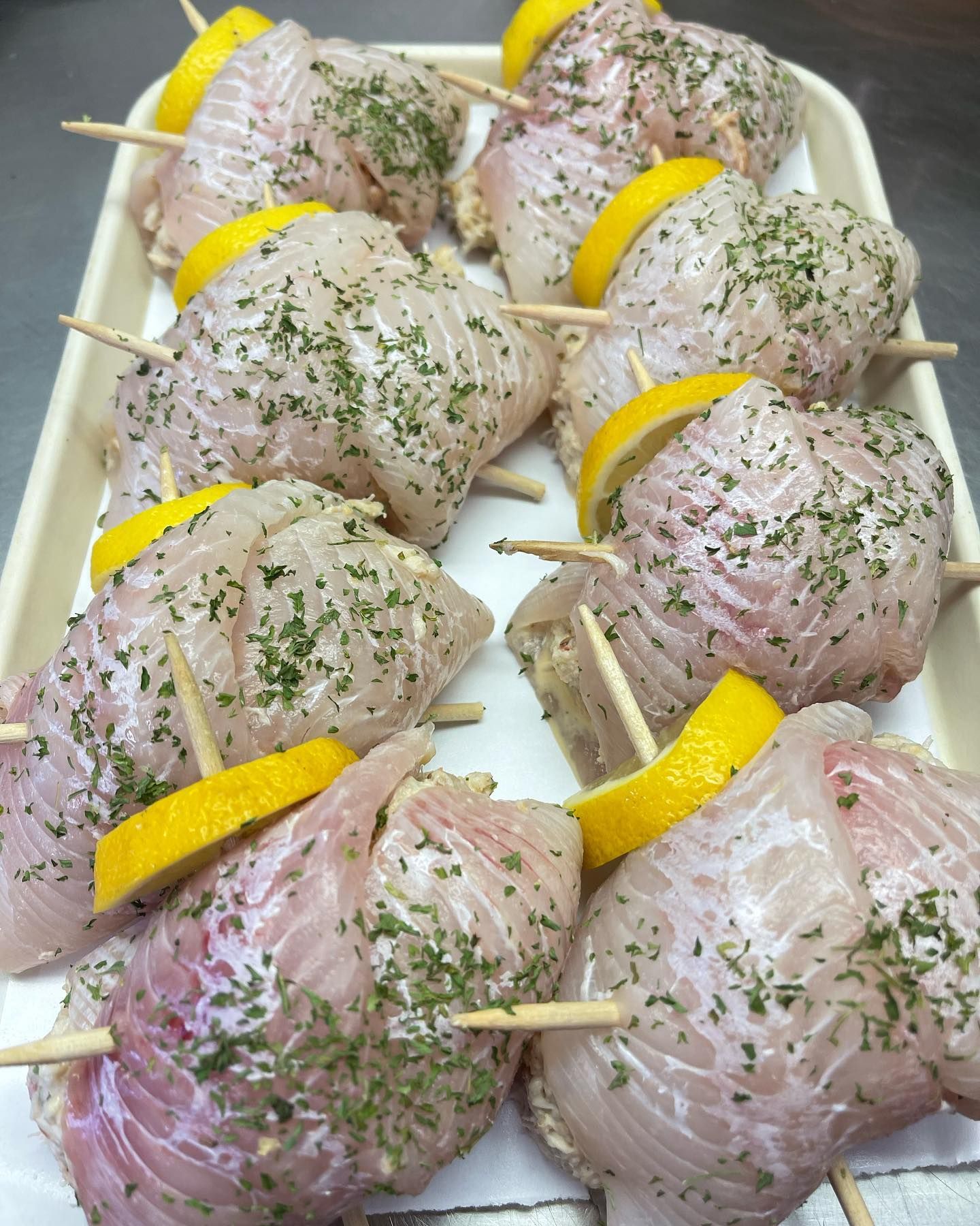 Raw fish rolls on a tray, skewered with toothpicks, garnished with lemon slices and herbs.