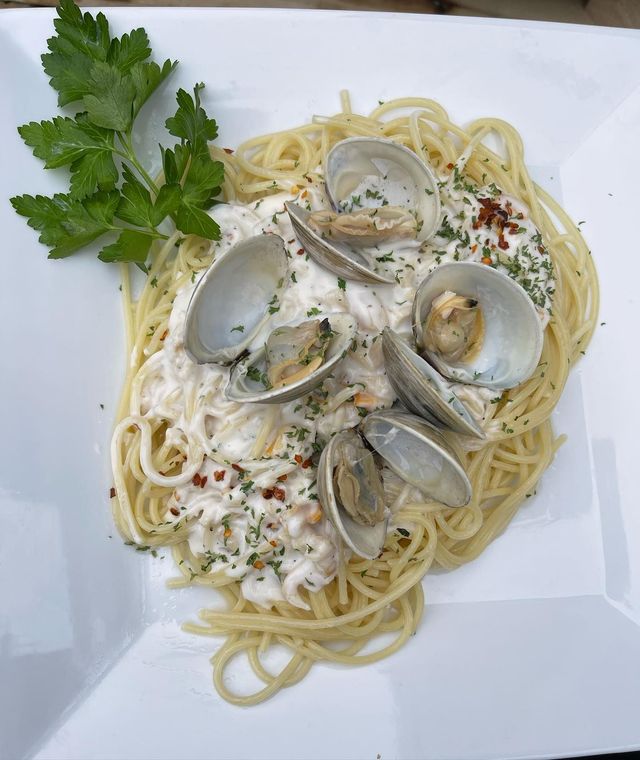 Spaghetti with clam sauce, served on a white square plate, garnished with parsley and red pepper flakes.