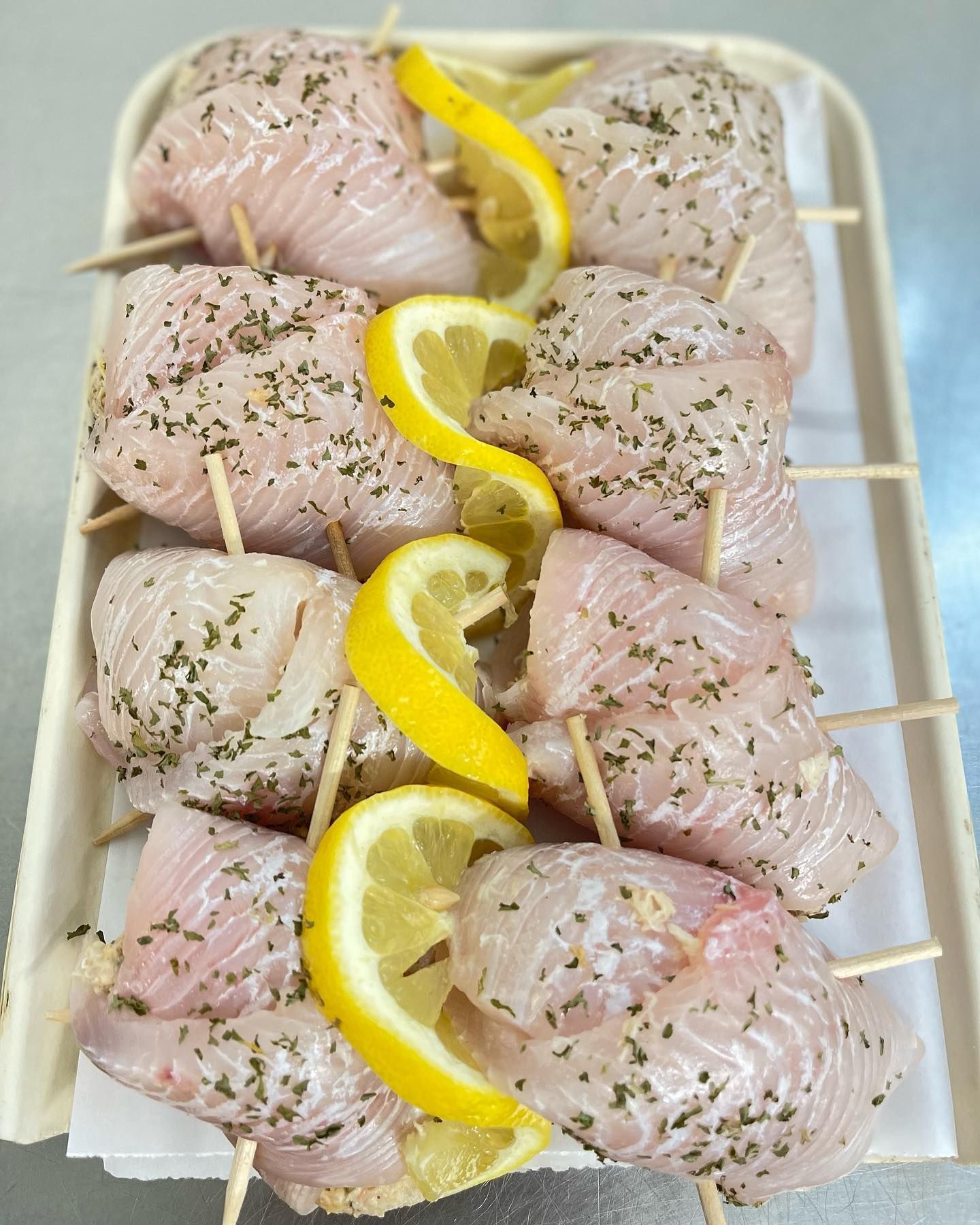 Raw fish skewers with lemon slices and herbs on a tray.