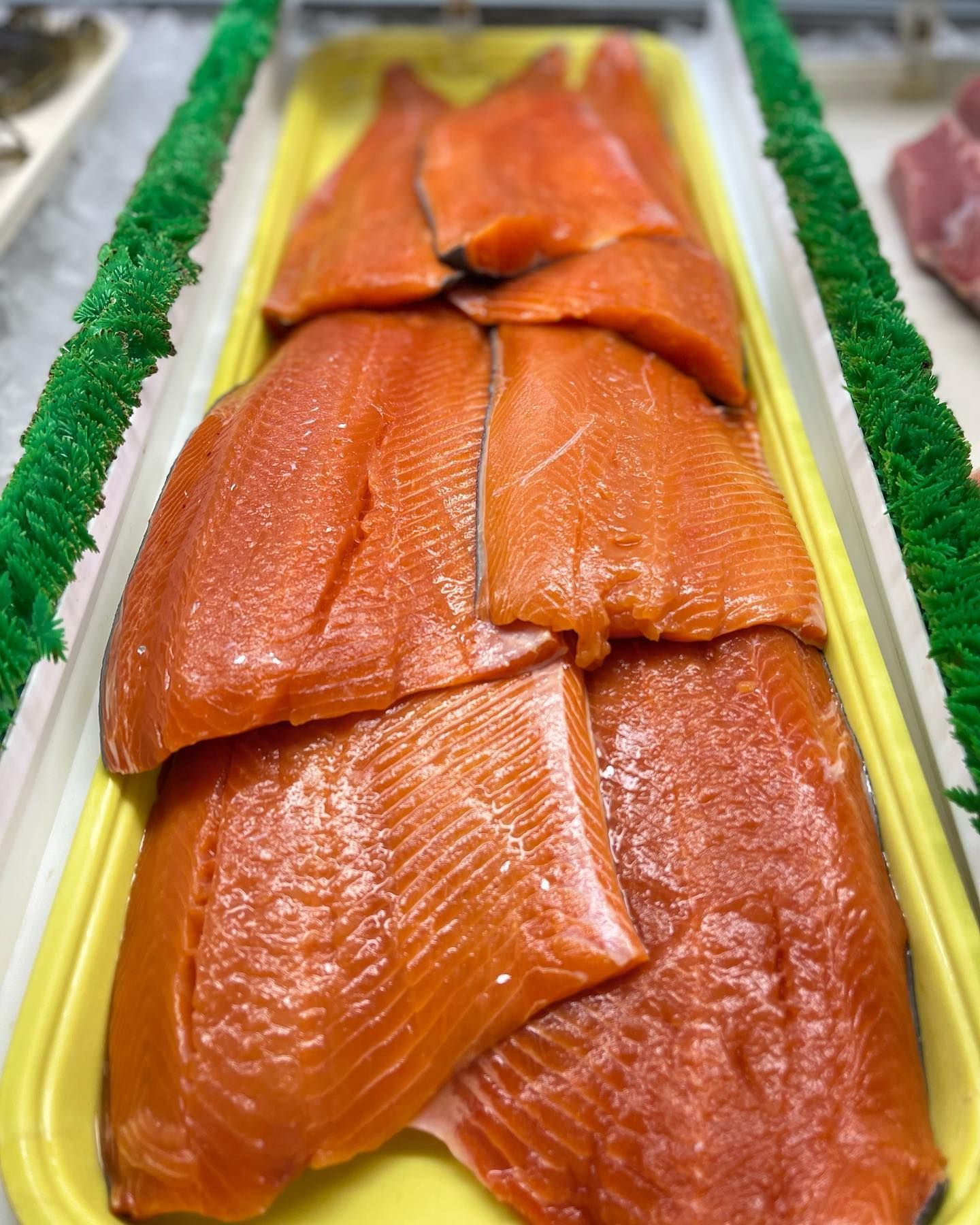Salmon fillets in a yellow tray at a market, vibrant orange color.