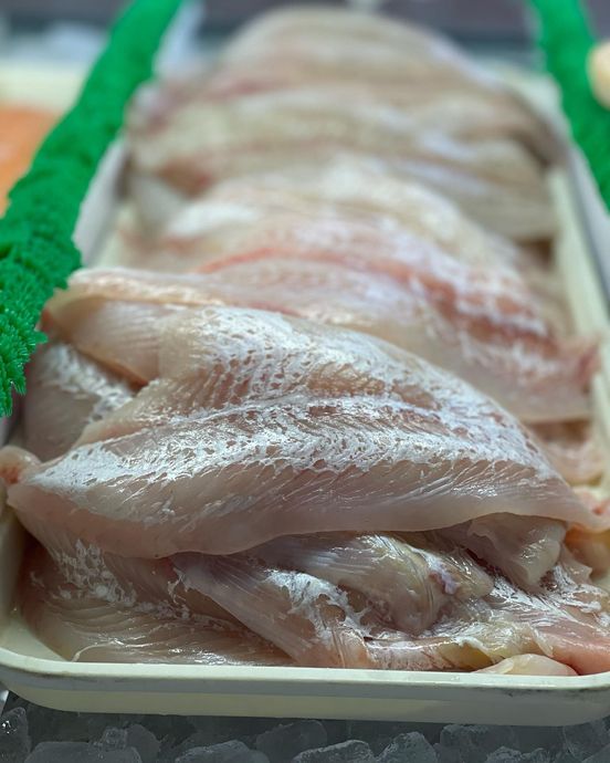 Raw, white fish fillets in a white tray at a seafood counter, with a green decoration on the side.