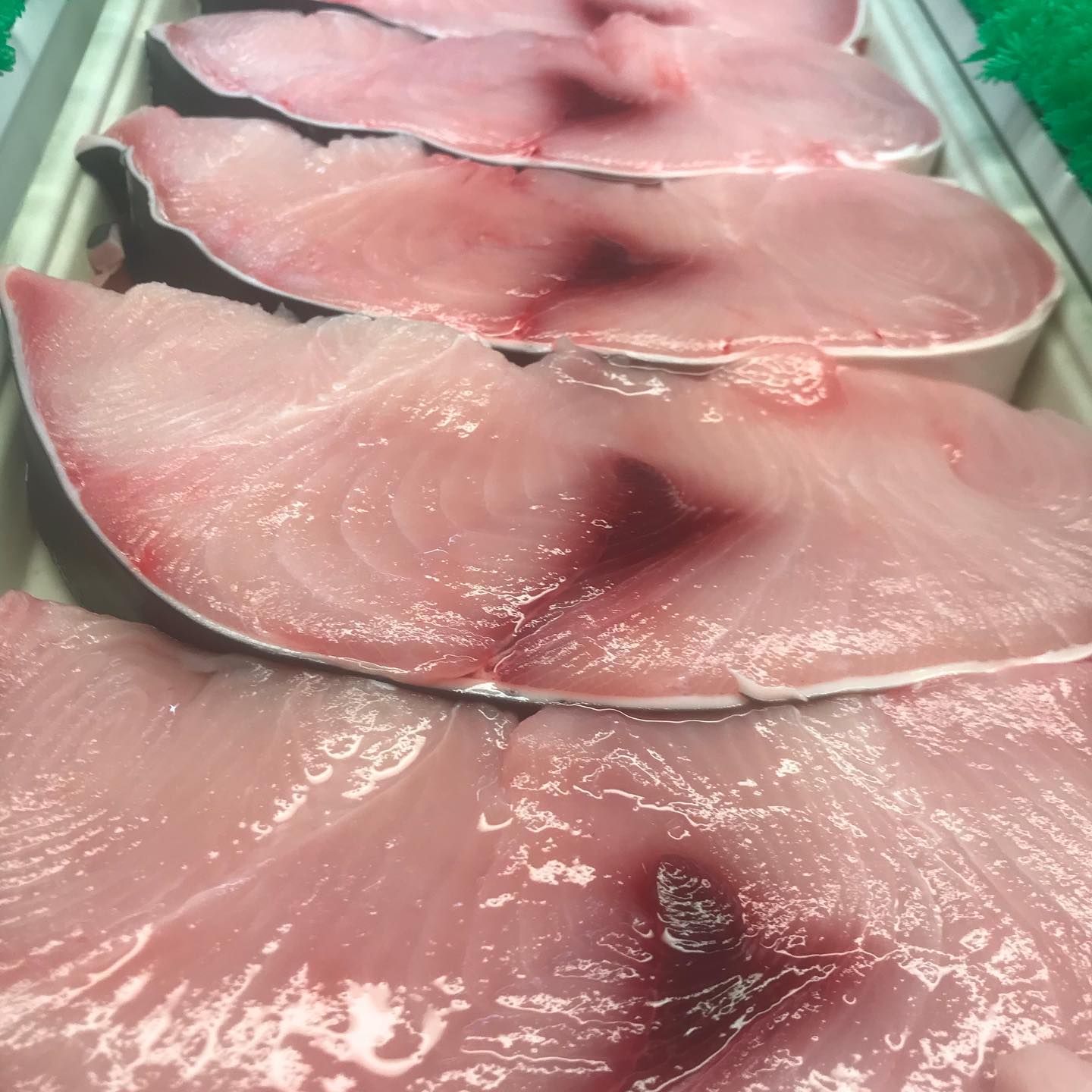 Freshly cut raw fish steaks arranged in a display case; pink flesh with dark red spots.
