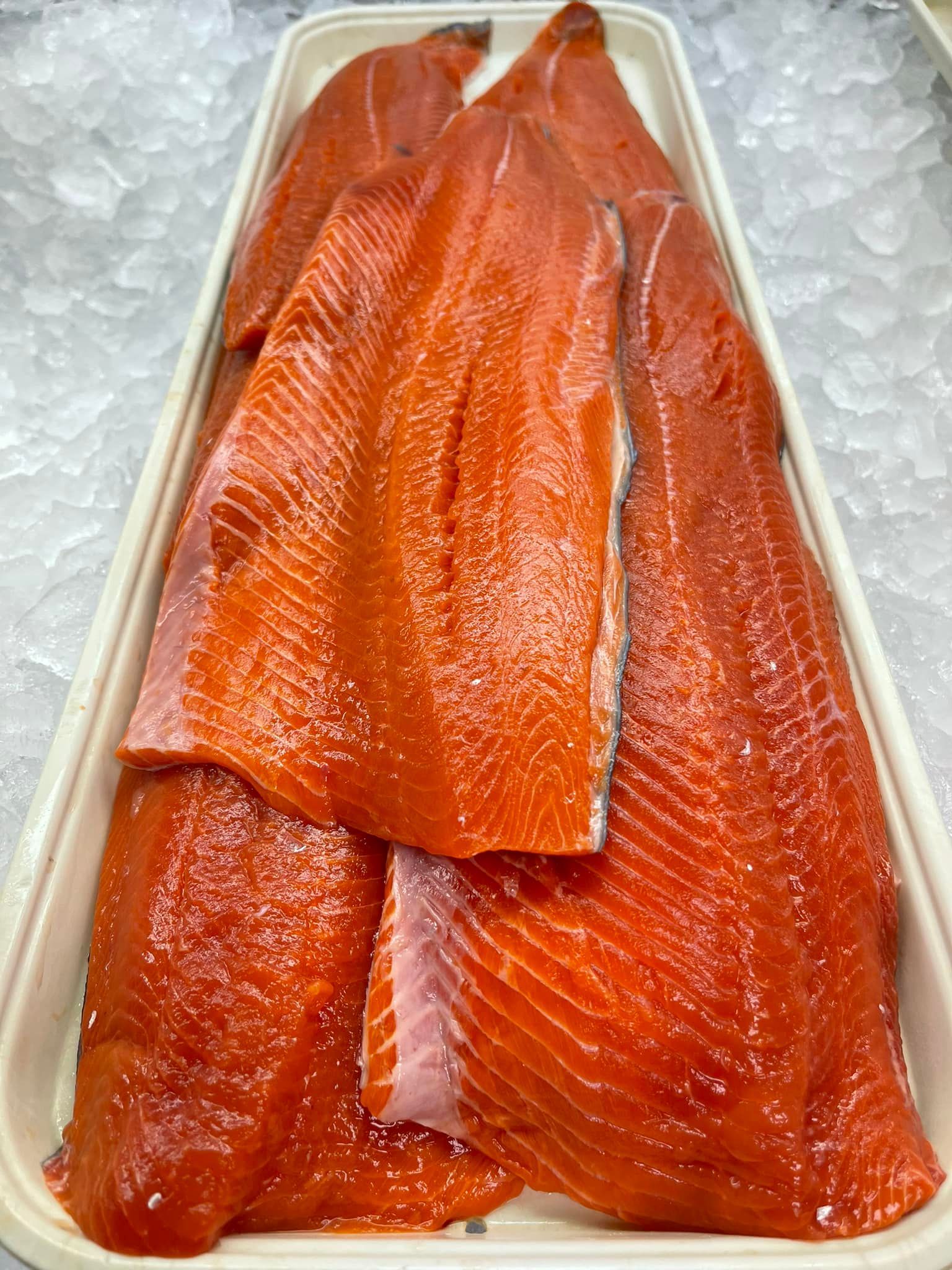 Raw salmon fillets on ice in a white tray; bright orange-red color.