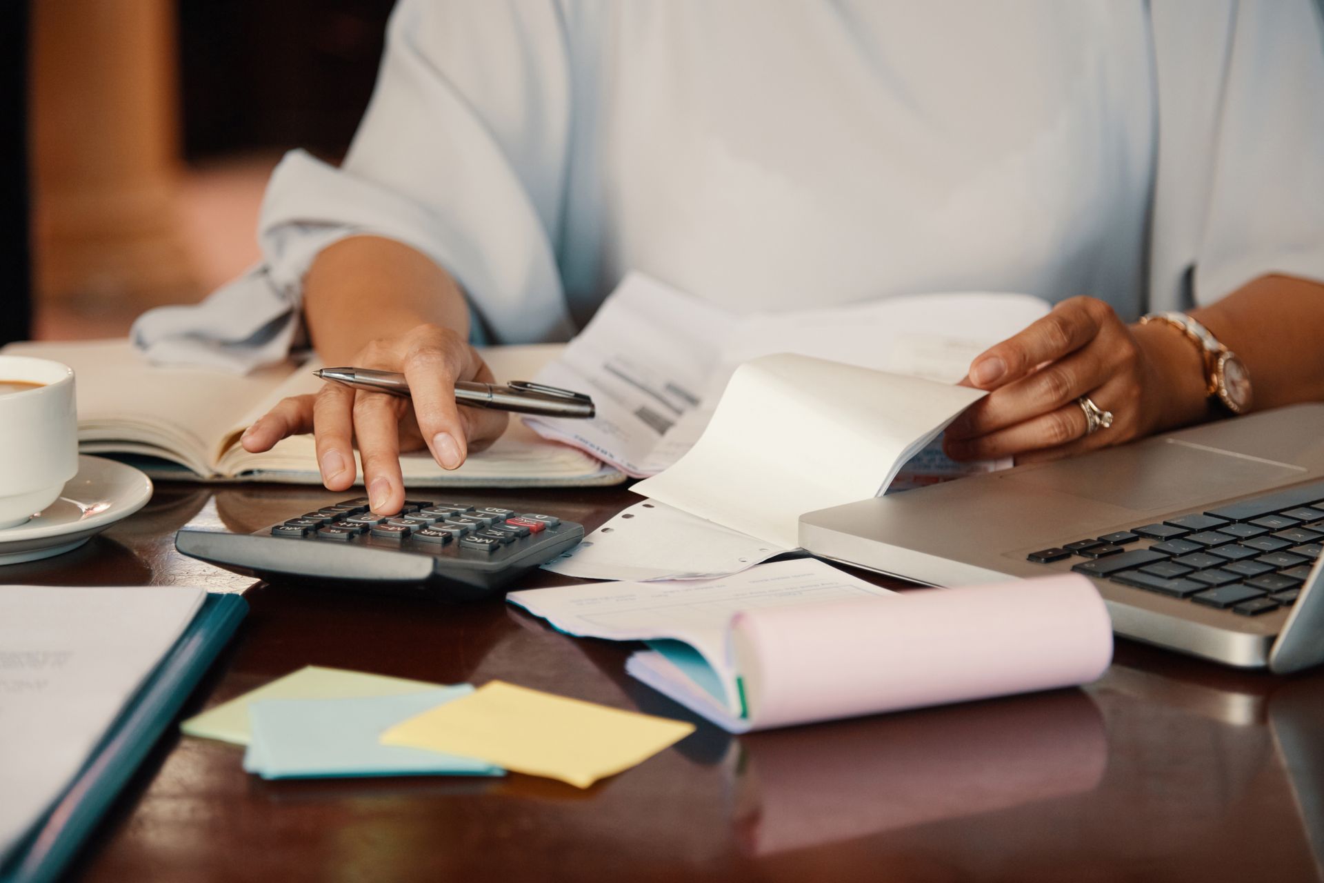 A woman is sitting at a desk using a calculator and a laptop.