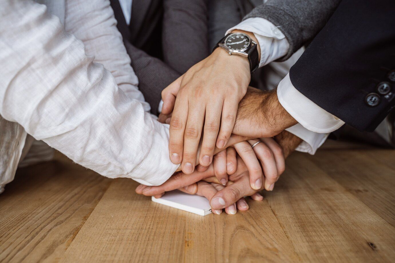 A group of people are putting their hands together on a wooden floor.