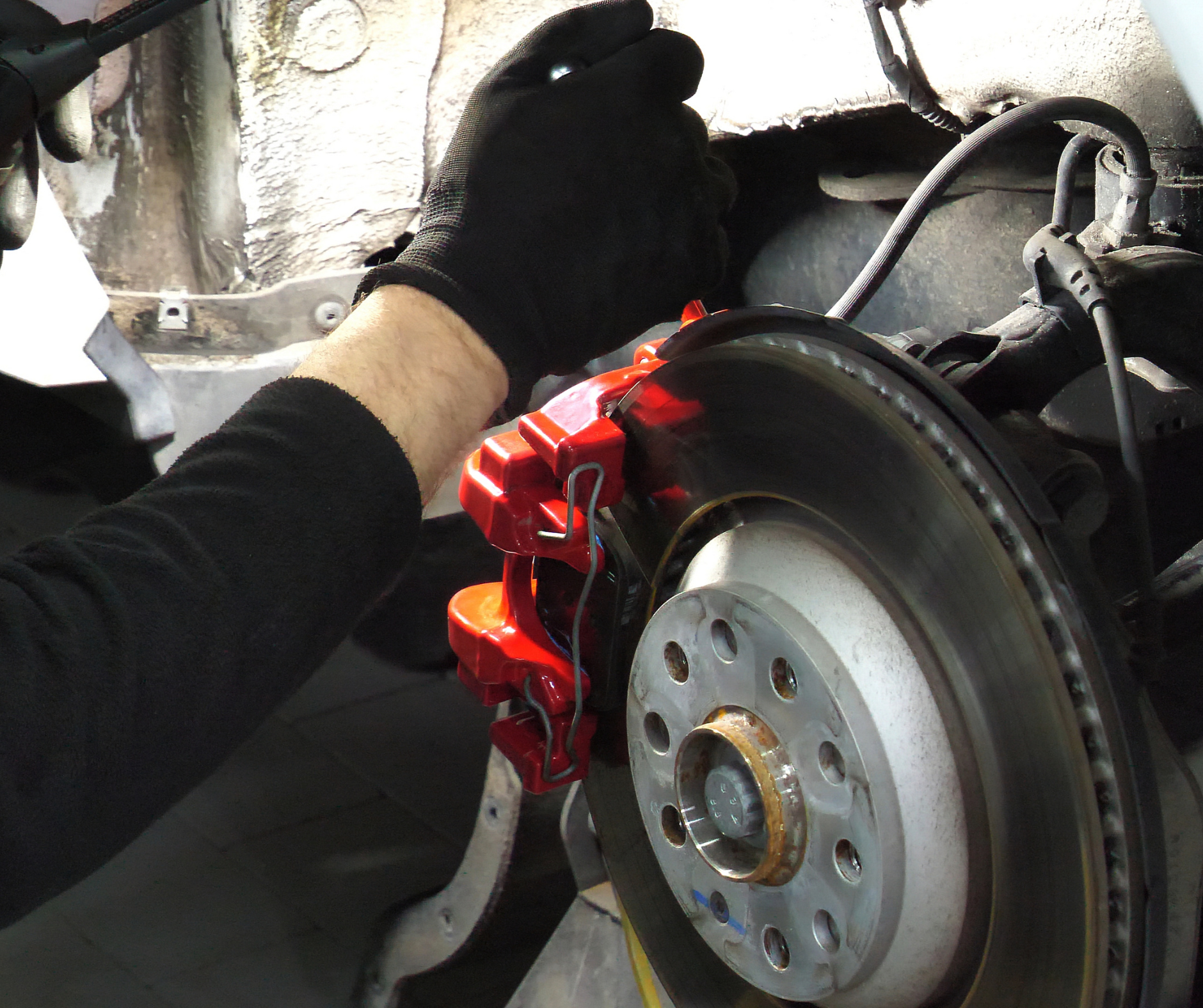 Person wearing a black glove working on a car's red brake caliper and rotor.