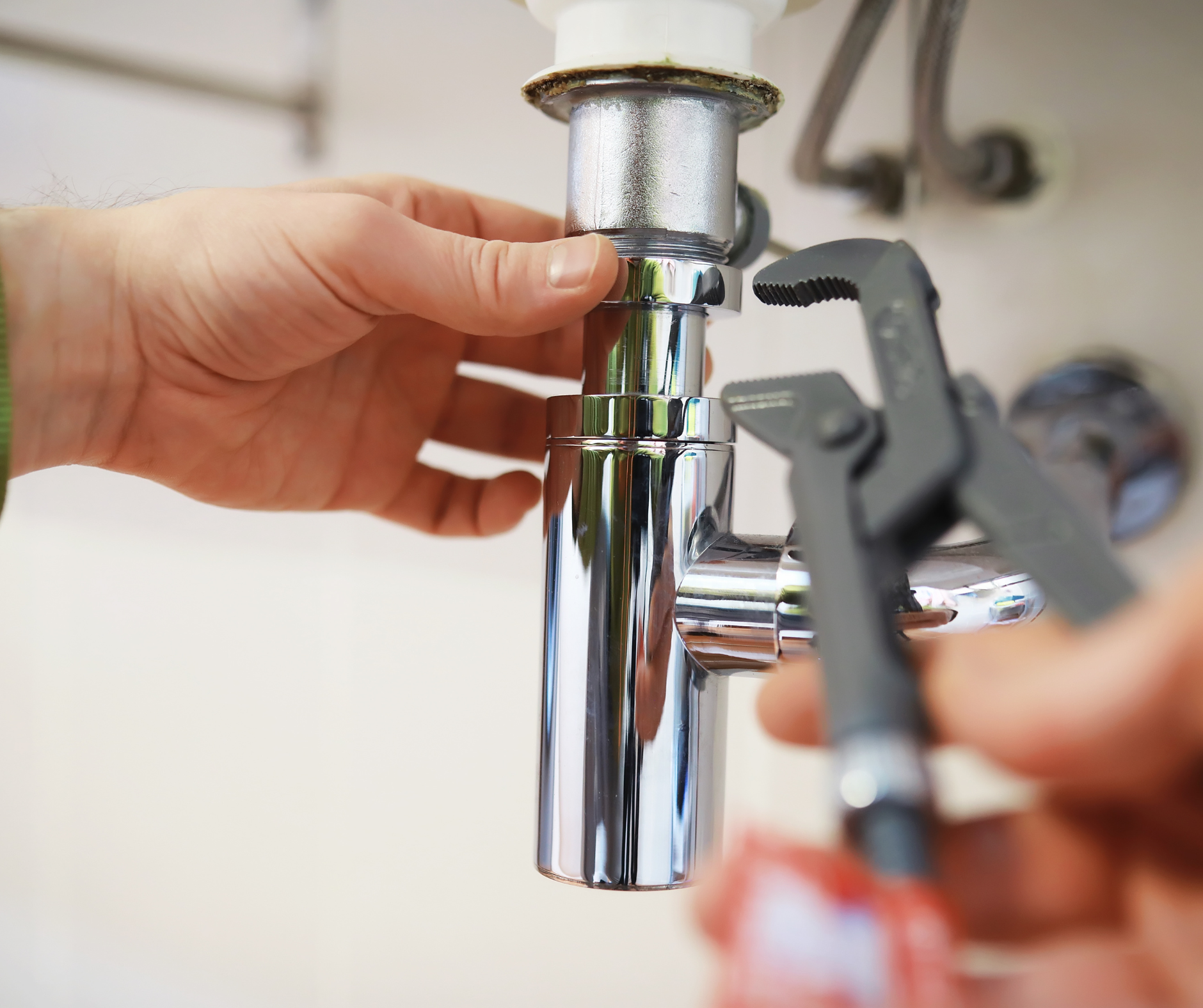 Plumber using a wrench to work on a chrome sink drain under a sink.