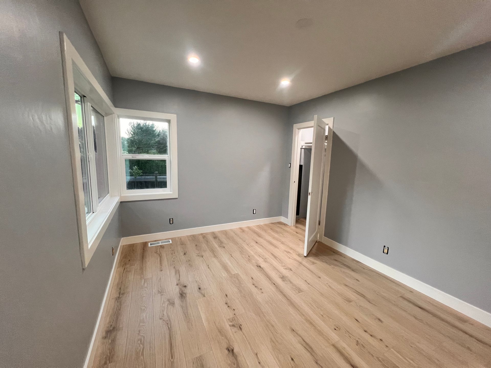 Empty gray room with wood floor, recessed lights, and an open door to a hallway
