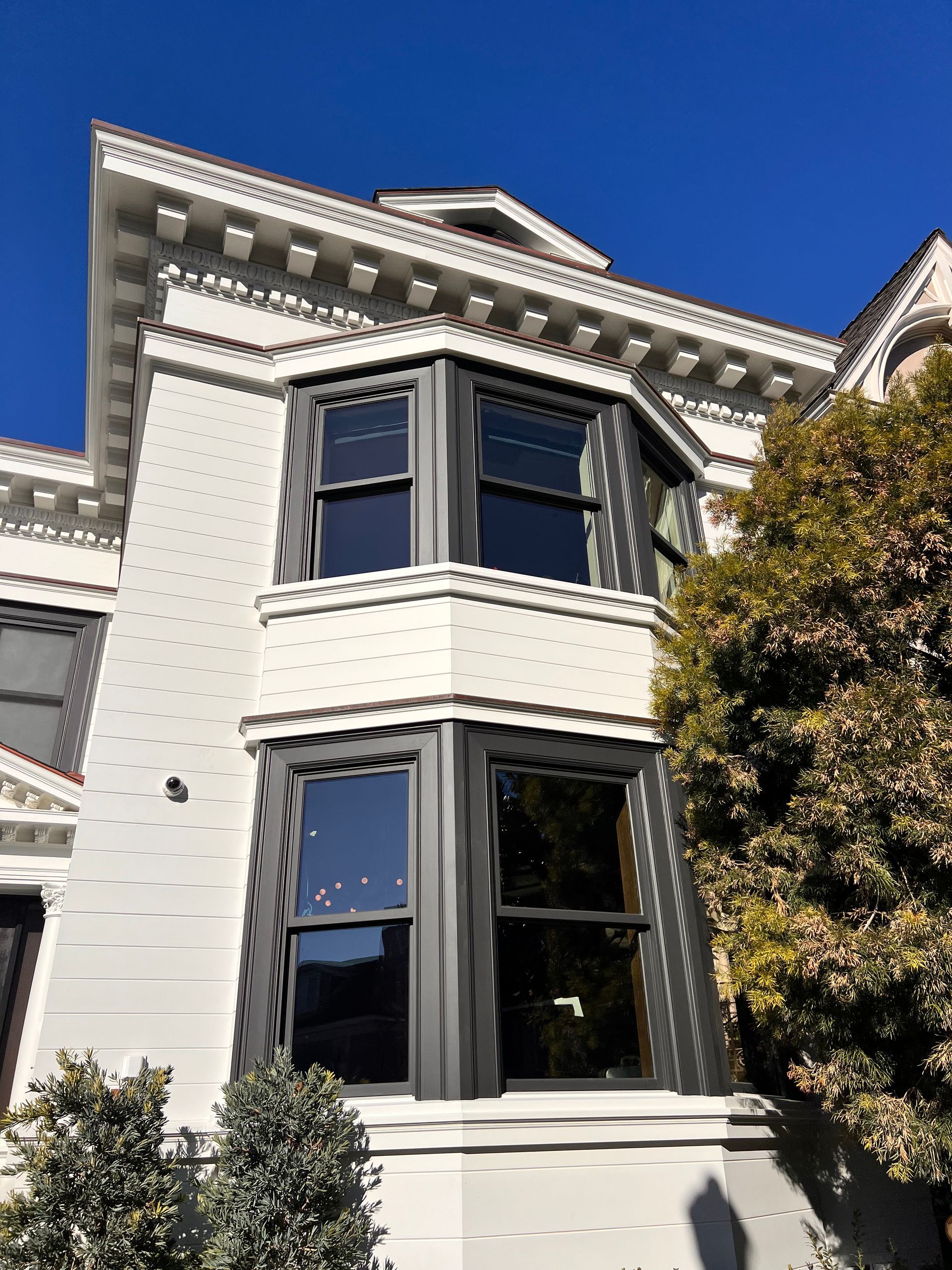 Victorian house facade with bay windows, white trim, and a blue sky above
