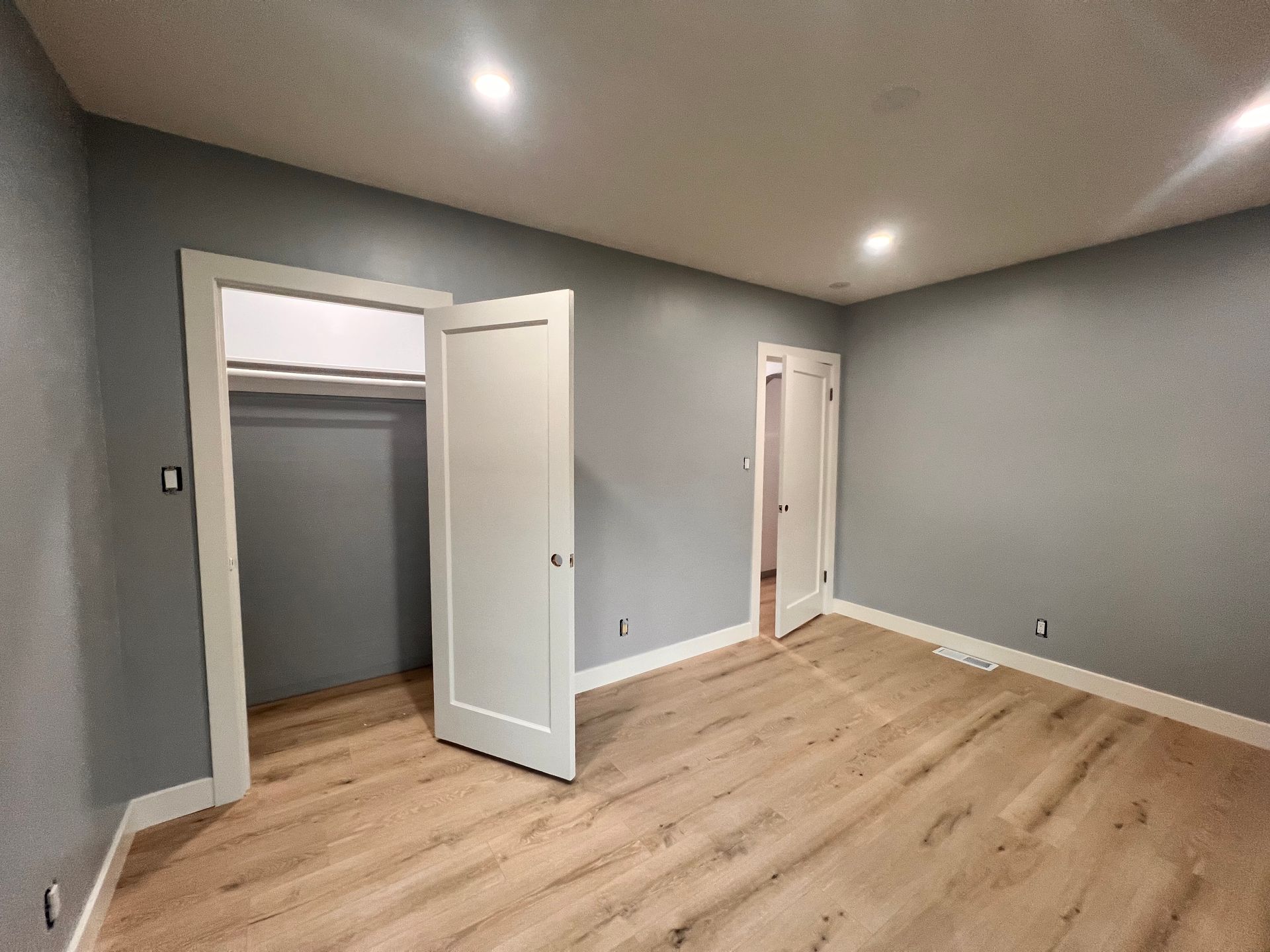 Empty gray room with light wood floors, recessed lights, and open closet and doorway.