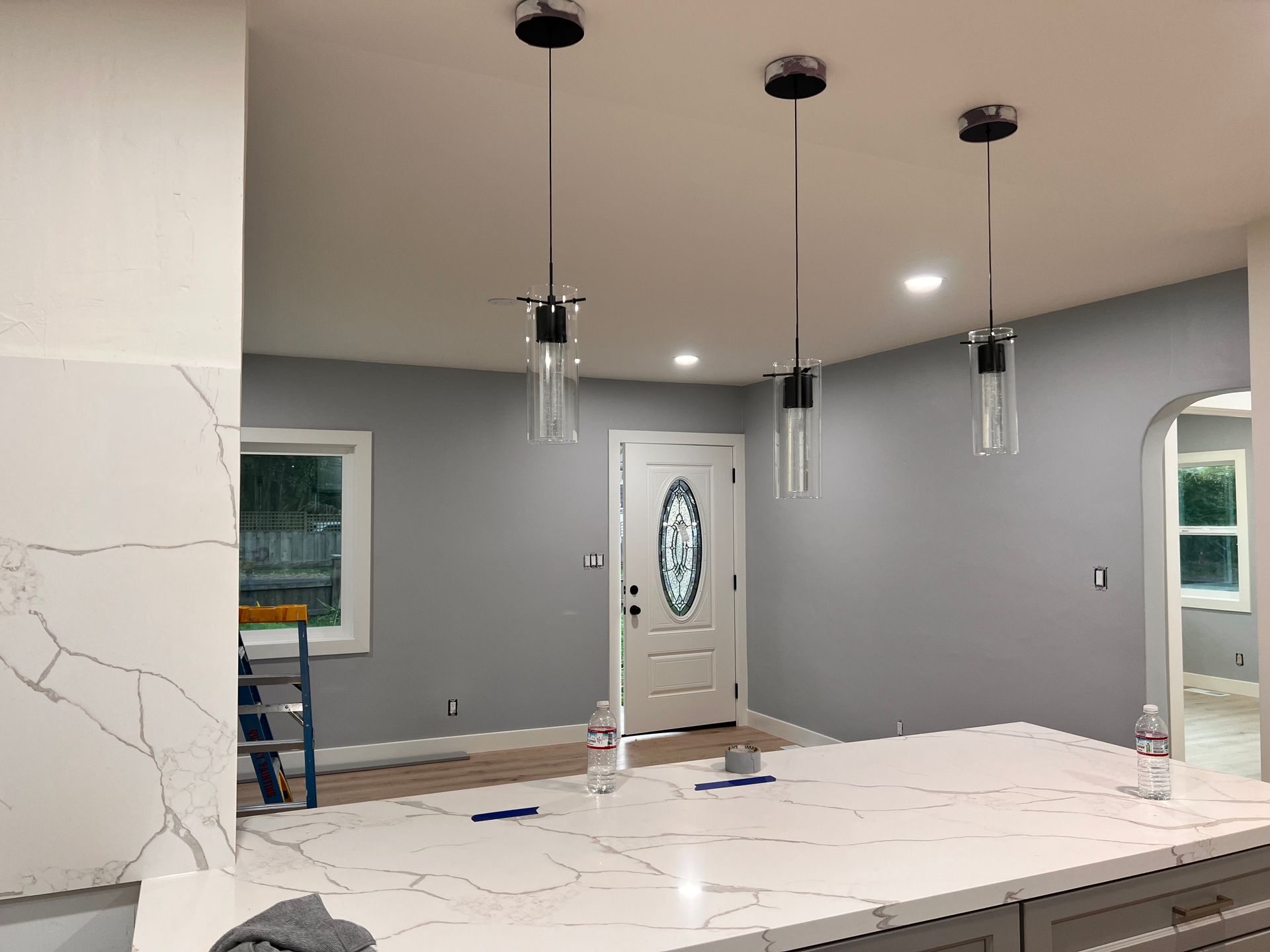 Modern kitchen interior with white marble island, gray walls, pendant lights, and a front door in back