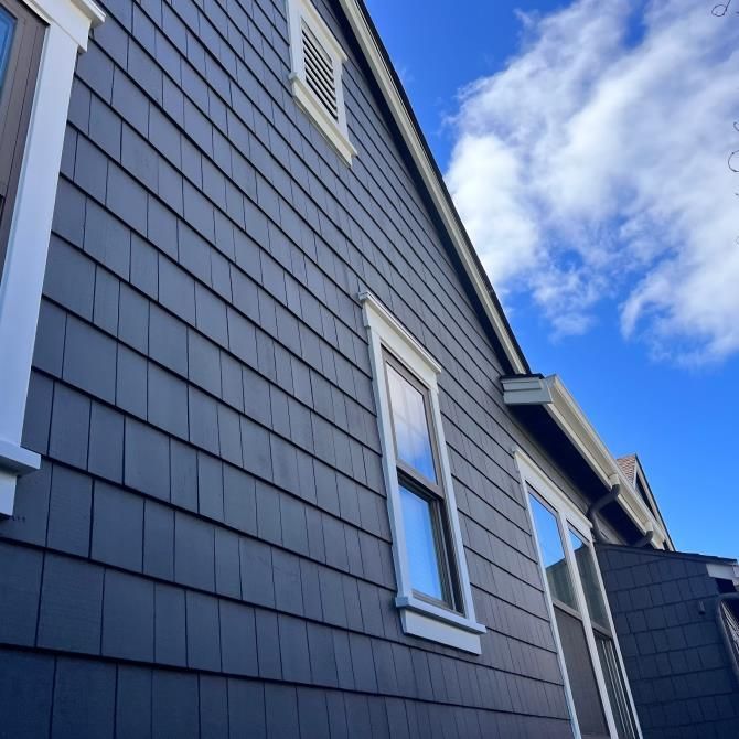 Blue house siding with white-trimmed windows against a bright sky