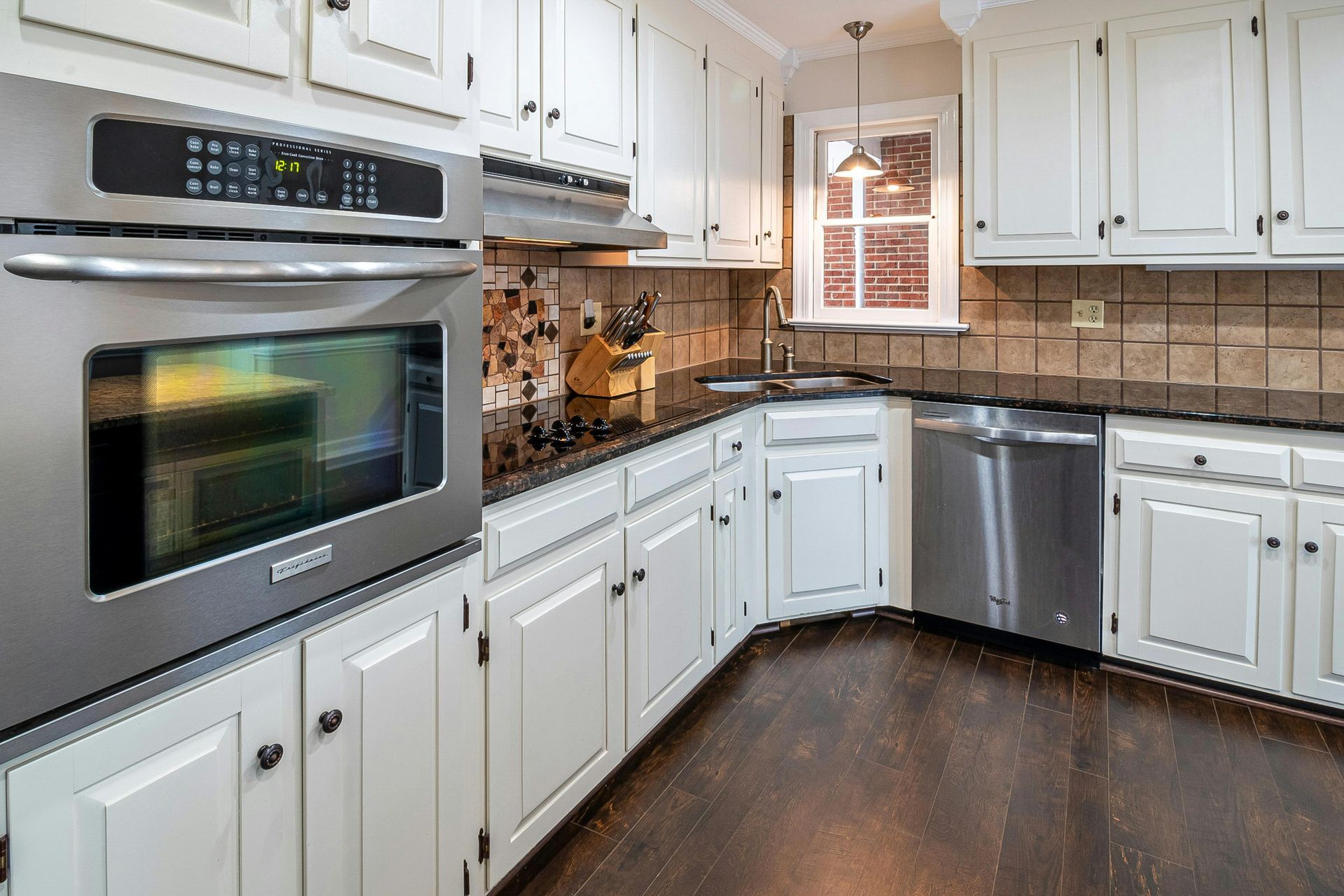 Bright white kitchen with stainless steel appliances, dark wood floor, and tan tile backsplash