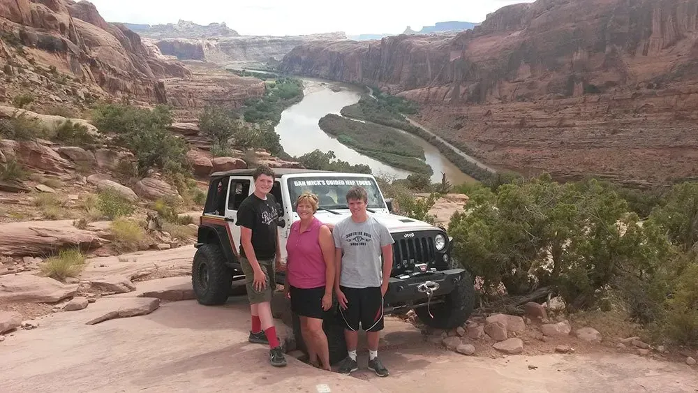 a group of people standing in front of a jeep with a river in the background