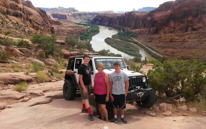 a group of people standing next to a jeep with a river in the background .